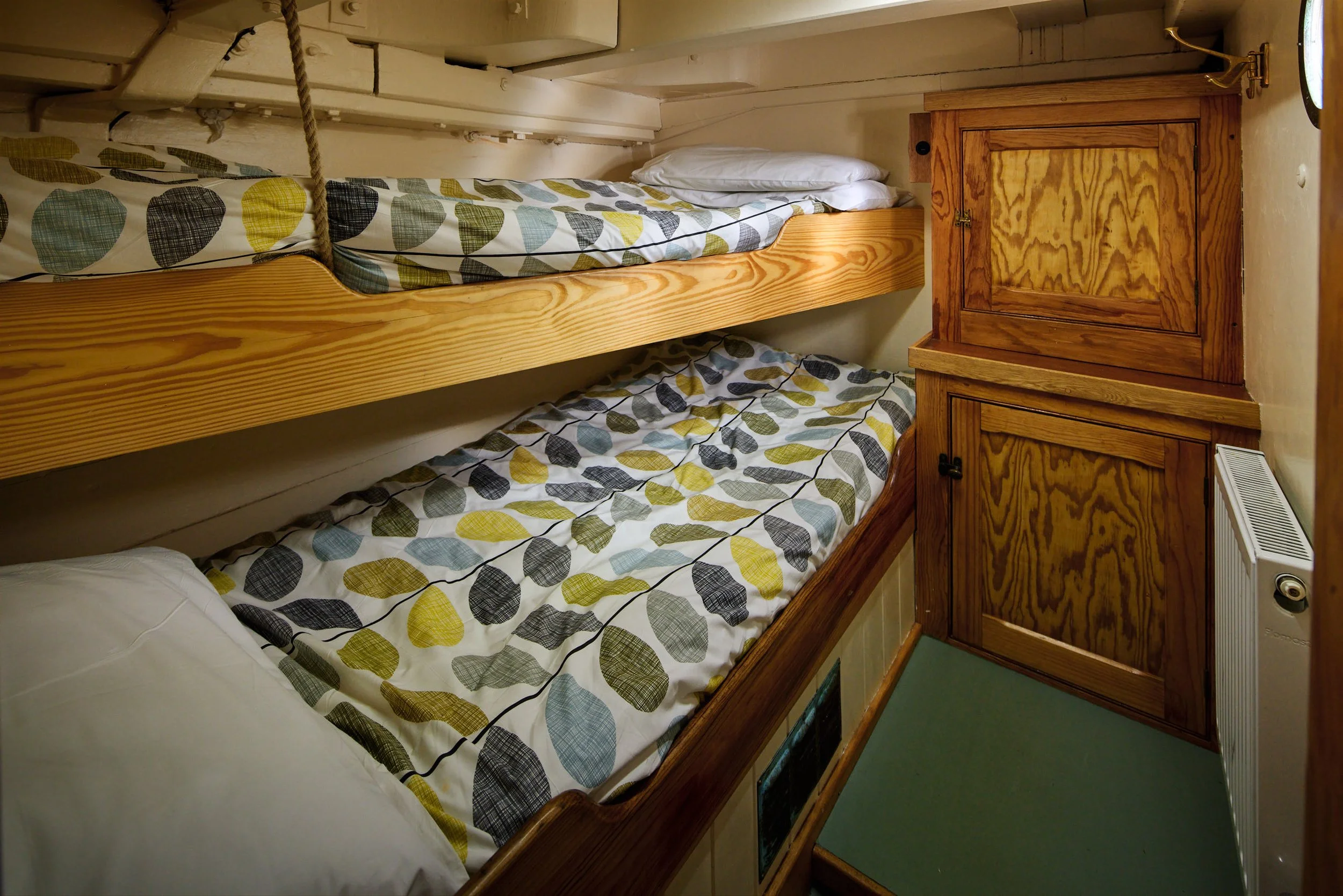 Bunk beds with patterned bedding, surrounded by wooden furniture and a small lamp on the side.