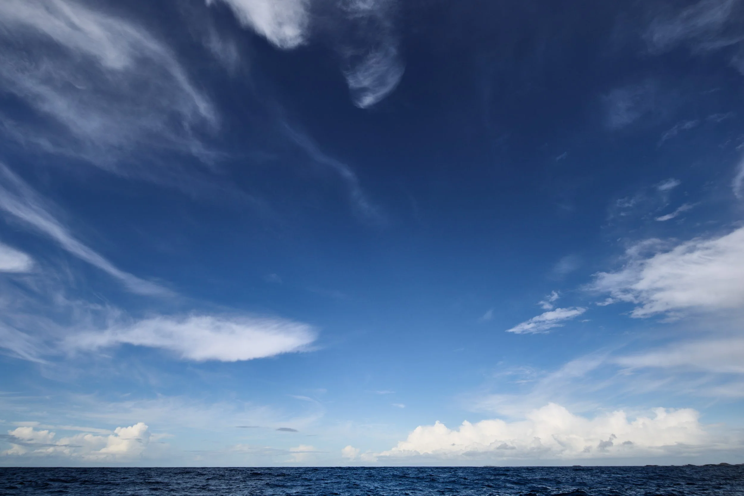 A wide view of the ocean with some clouds in the blue sky.