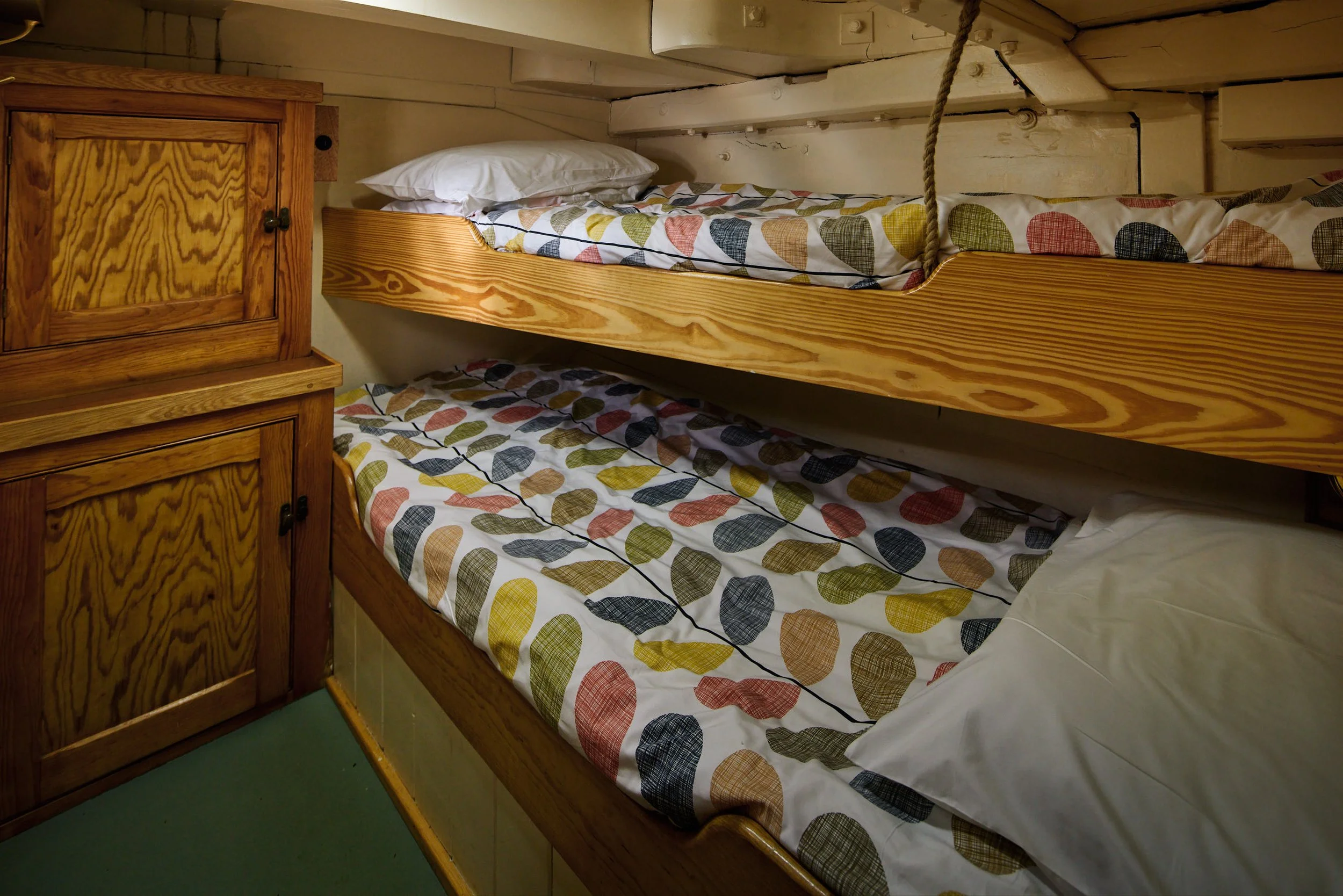Bunk bed with a mattress, pillow, and a colorful leaf-patterned comforter in a rustic room with wooden cabinets and beige paneling.