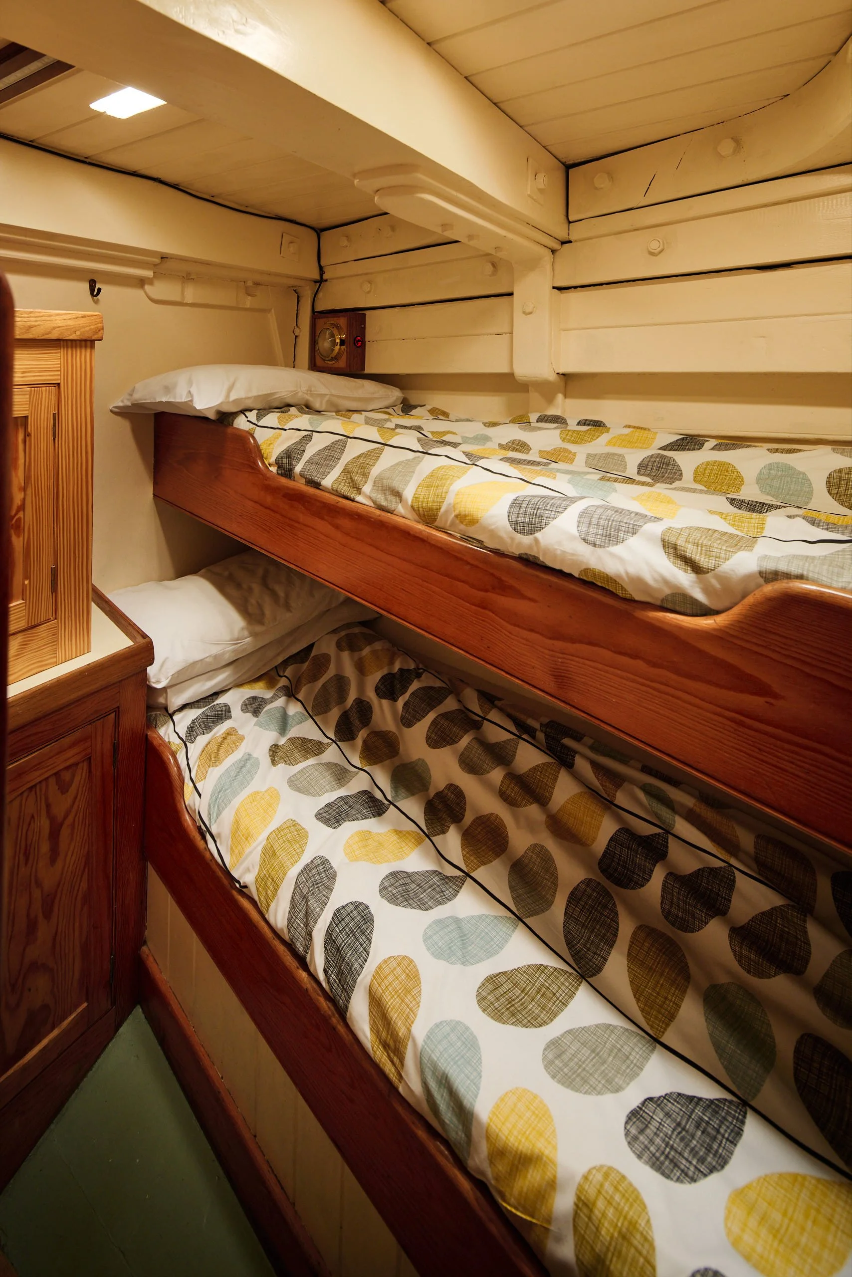 Bunk bed with a wooden frame and printed bedspread with yellow, gray, and black polka dots in a cozy wooden room.