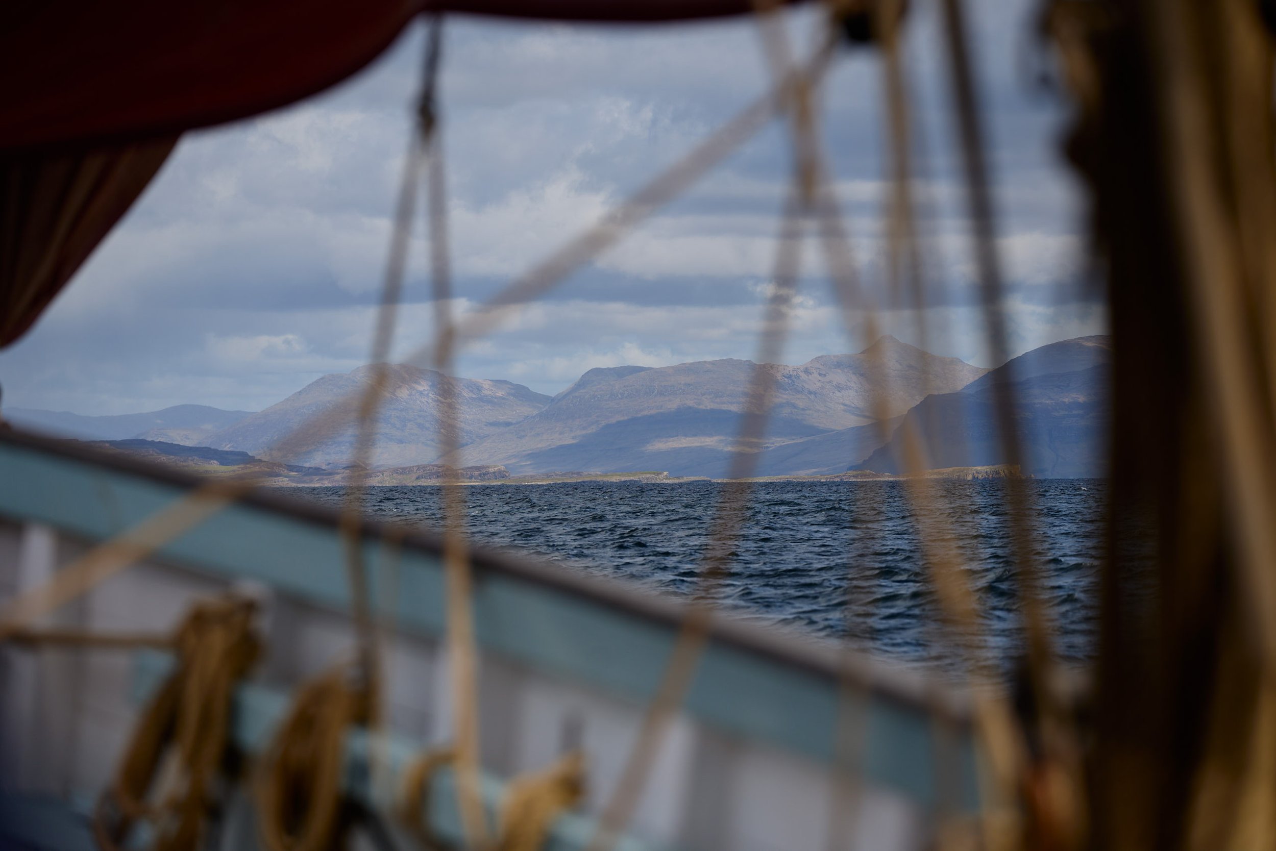Landscape view of mountains across a body of water, seen through a mesh or netting, with a part of a boat or structure in the foreground.