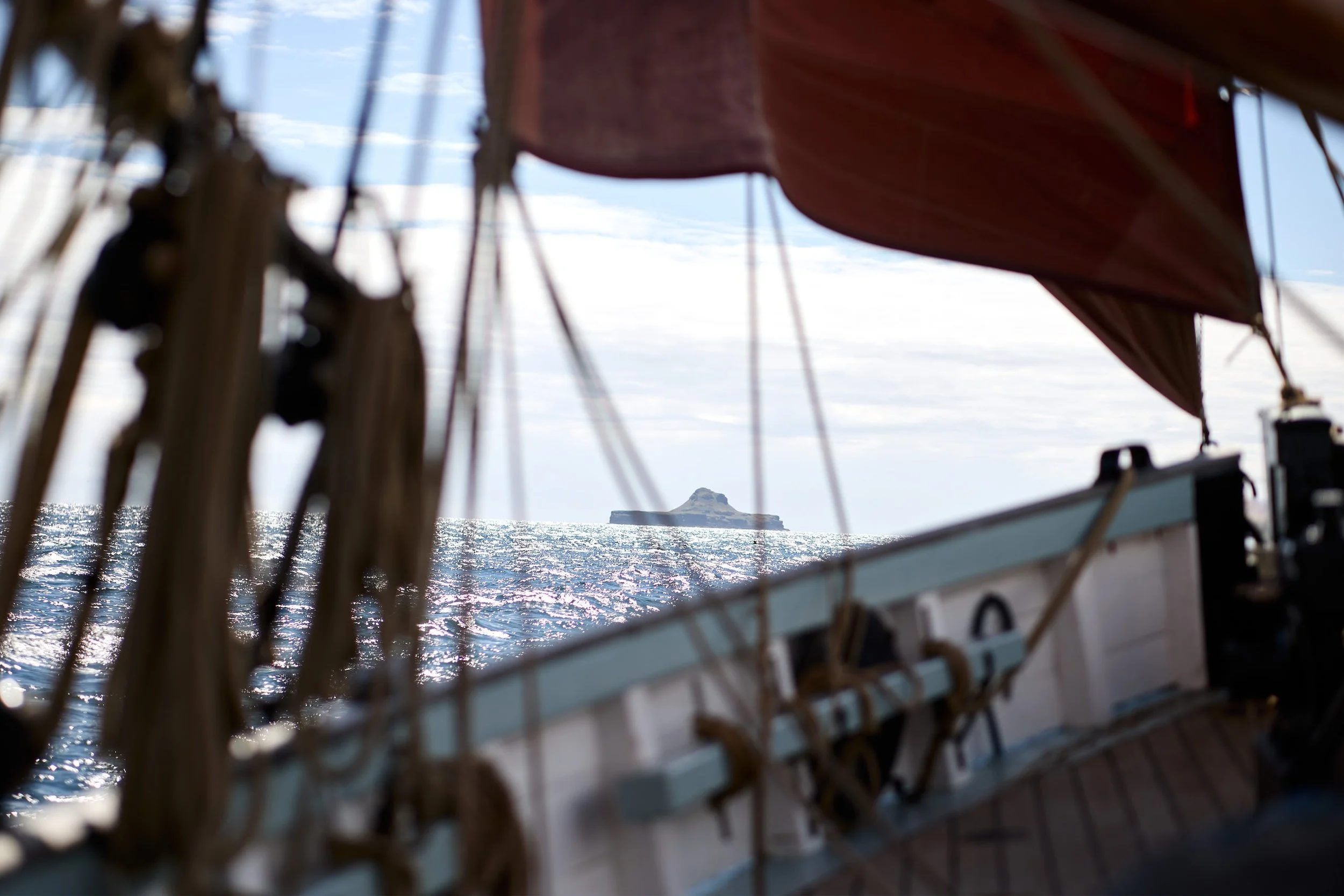 View from a boat showing a distant island or mountain through the boat's railing and mast.