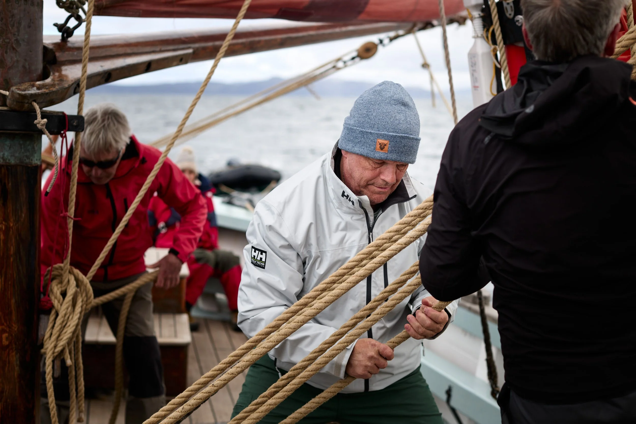 People on a ship holding ropes and participating in a nautical activity.