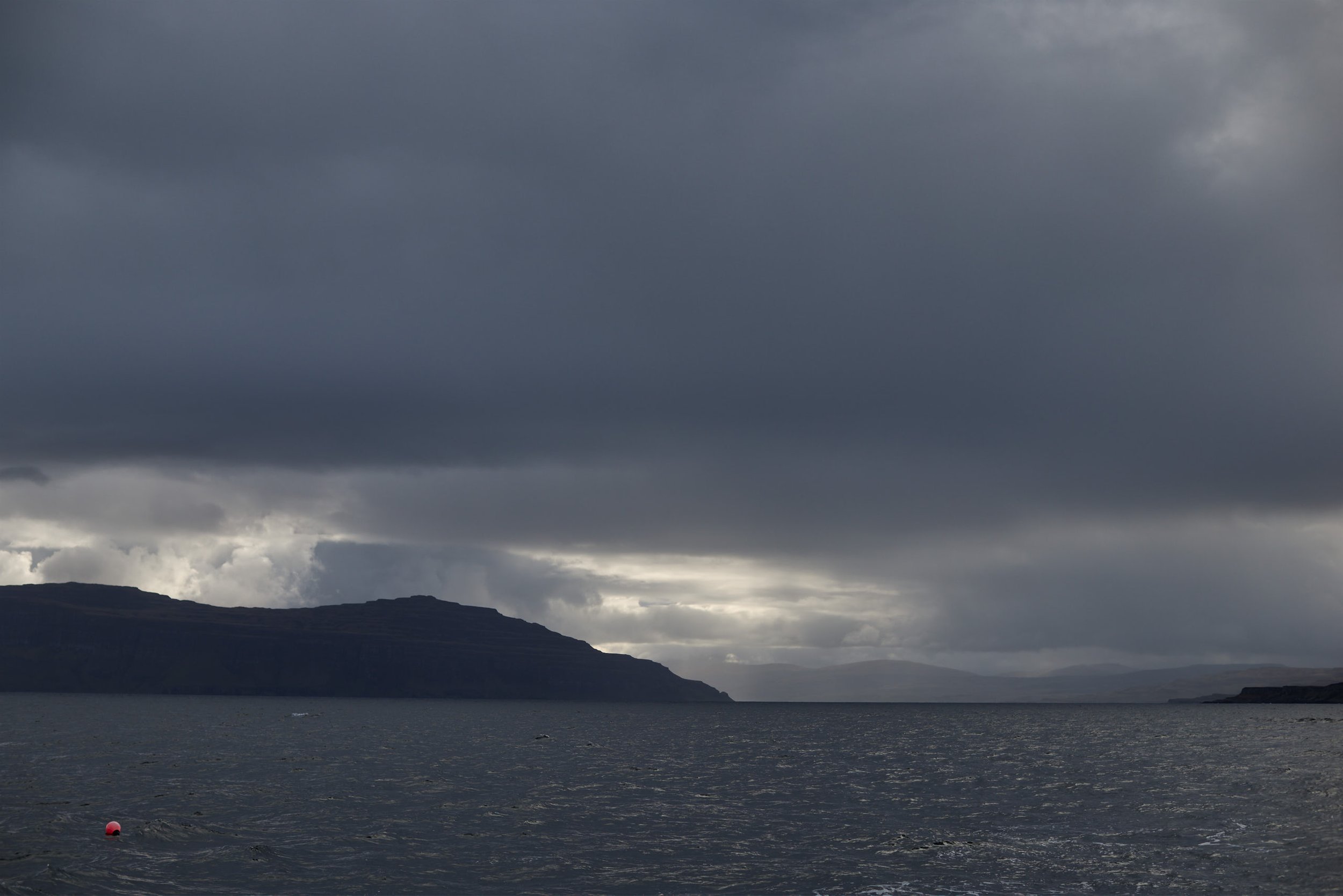 Dark stormy sky over a body of water with mountainous land in the distance.
