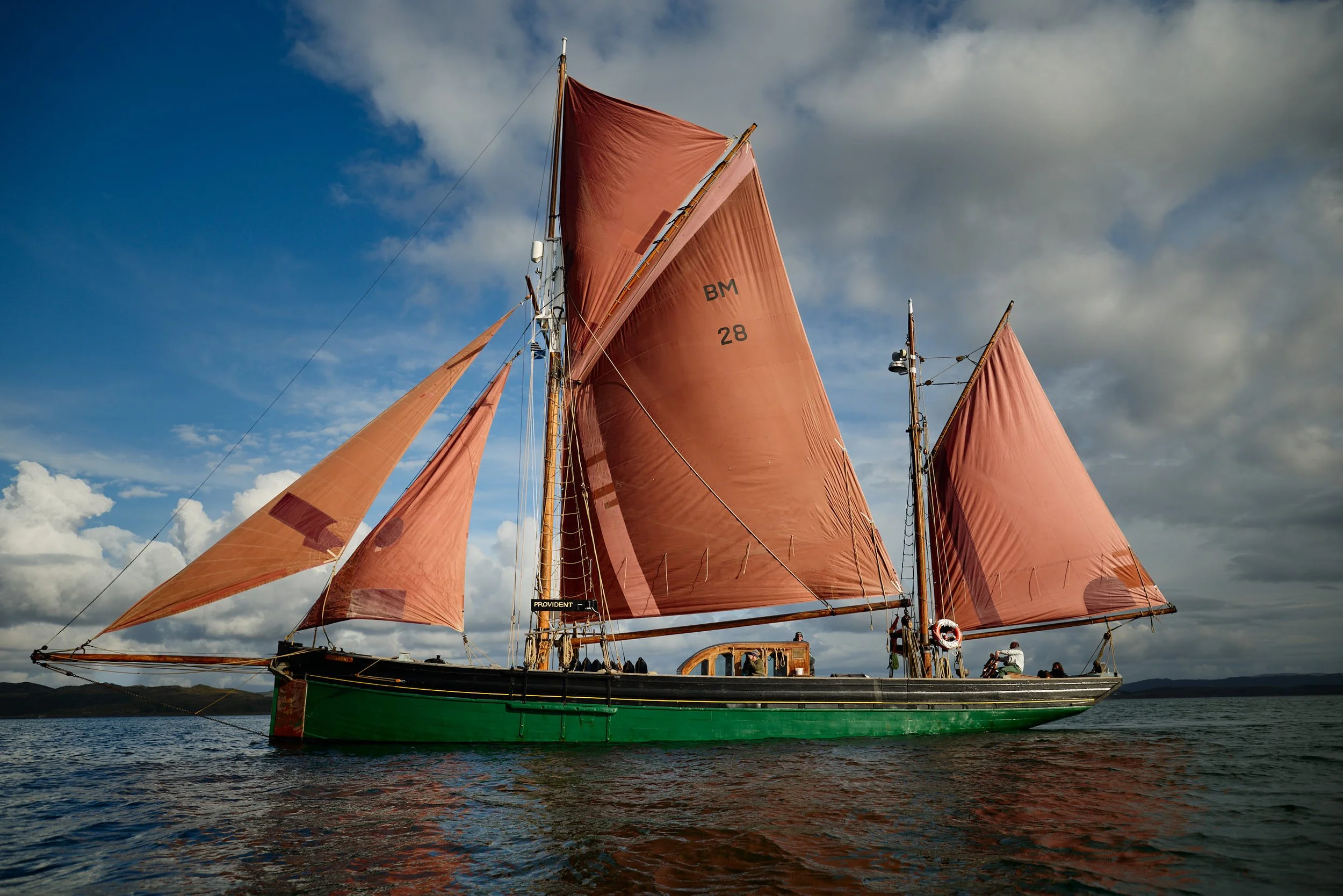 The classic sailing ship, Provident,  with orange sails floating on water under a partly cloudy sky.
