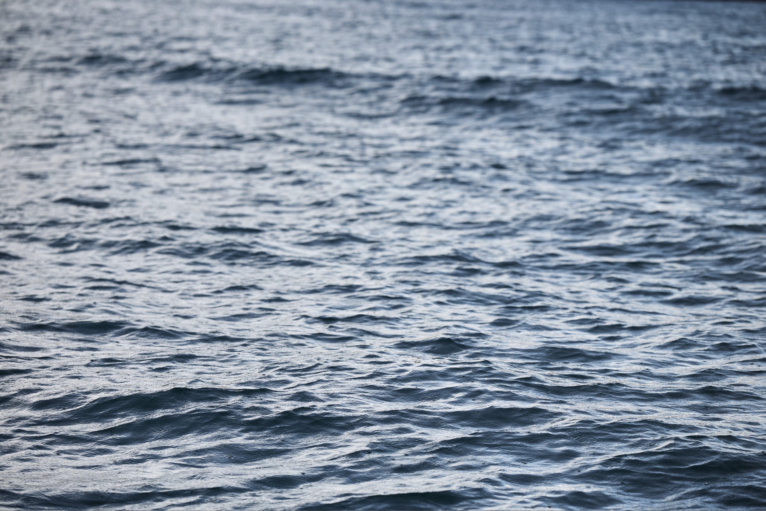 Open ocean with small waves and ripples under a cloudy sky.