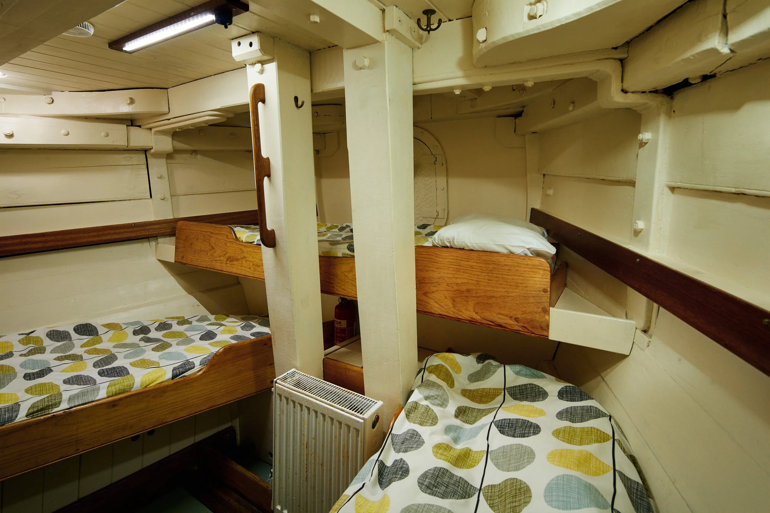 Bunk beds with wooden frames and patterned bedding in a small, cozy room, with a heater at the foot of one bed and various wall fixtures.