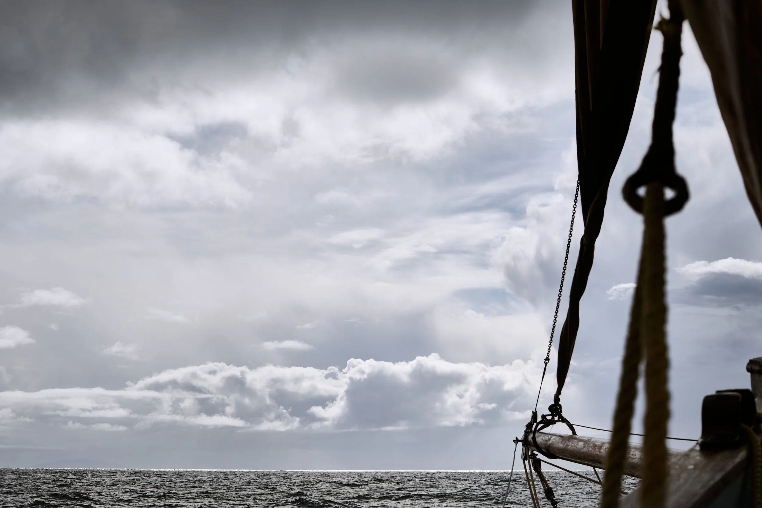 View from a sailboat on dark water under a cloudy sky, with part of the boat's rigging and sail visible on the right side.
