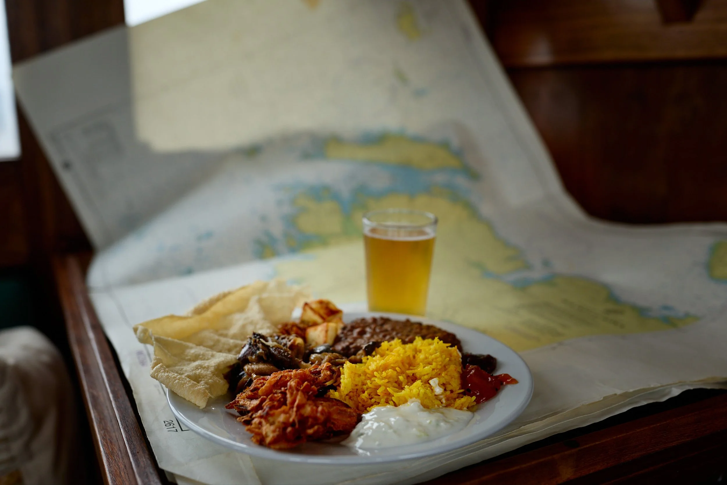 Plate of Mexican food with rice, beans, beef, chicken, chips, sour cream, and salsa, with a glass of beer in the background.