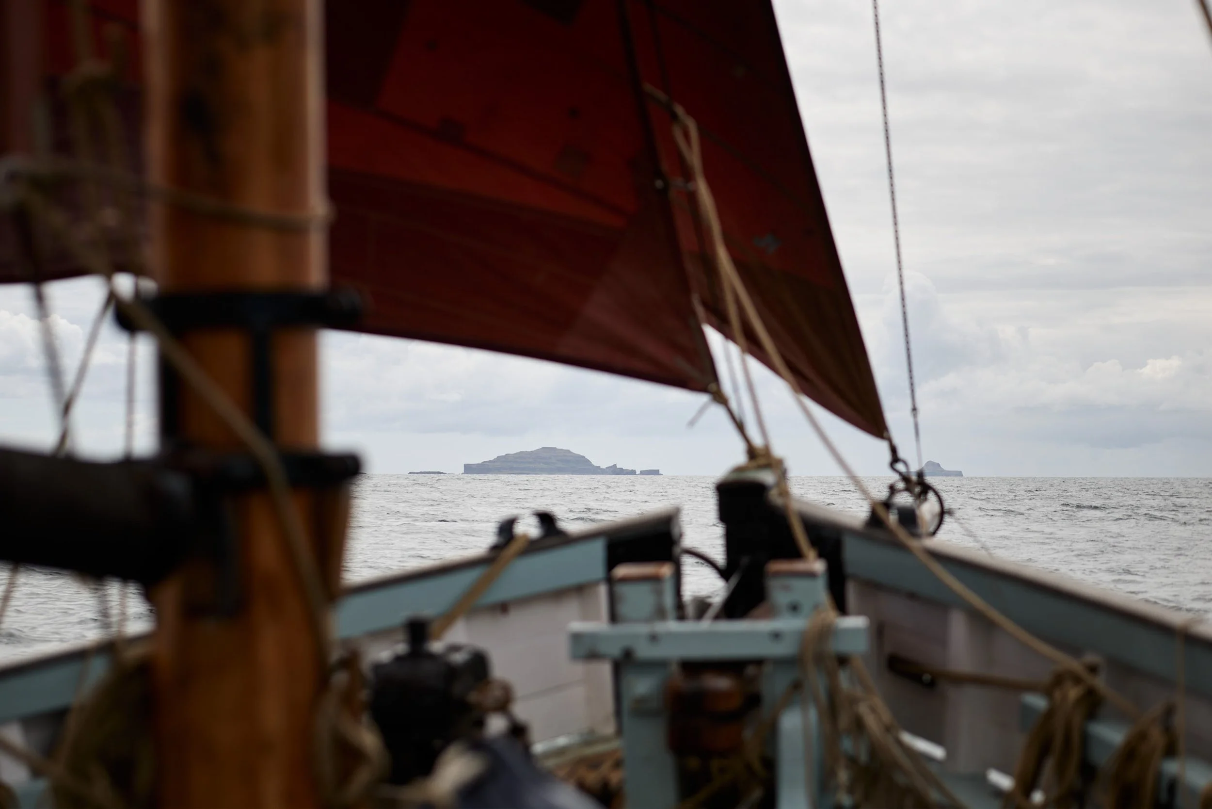 Close-up view of a boat's interior with wood framework and ropes, overlooking the water with distant landforms and cloudy sky.