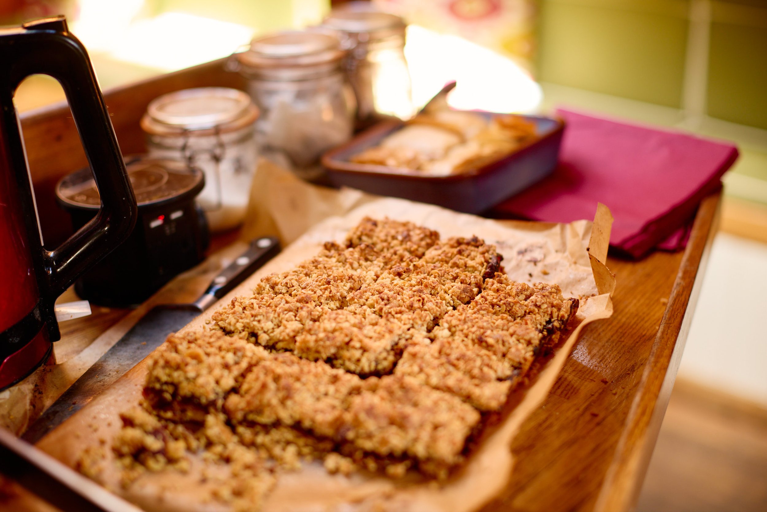 A tray of freshly baked crumb-topped dessert with a crumbly texture and golden brown color, placed on parchment paper on a wooden surface.