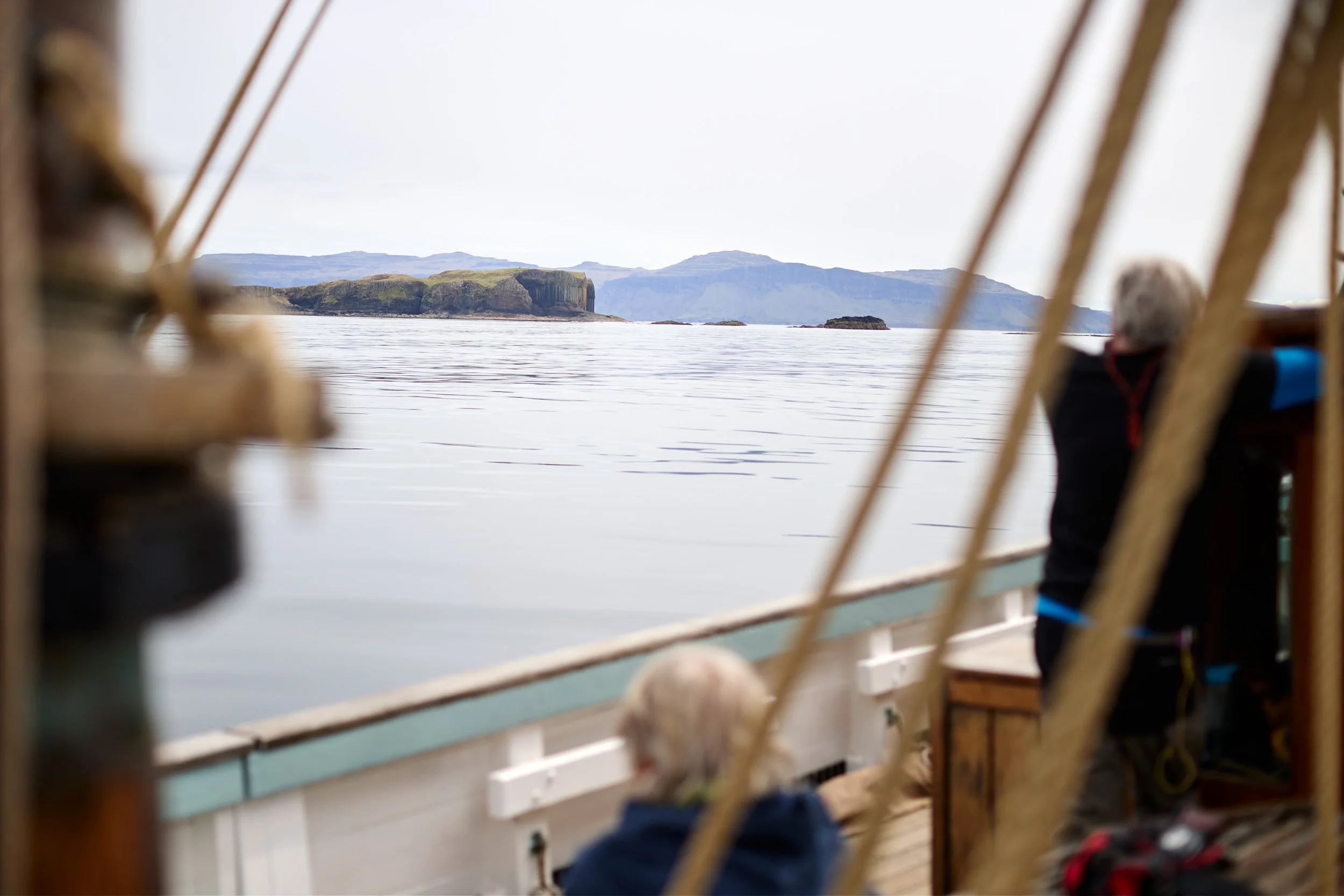 View of a body of water with rugged islands and mountains in the distance, seen through the wooden frame of a boat.