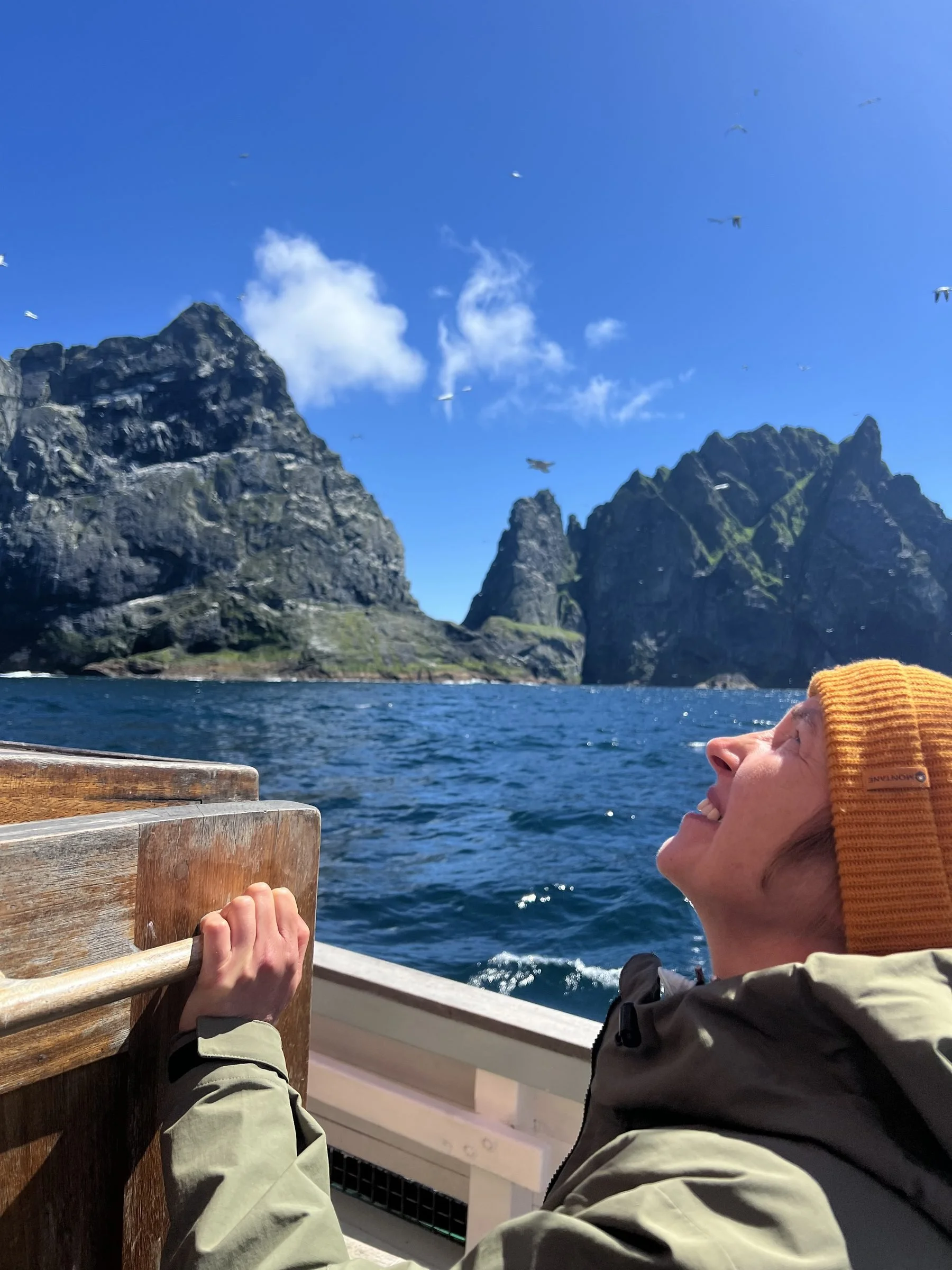Person wearing an orange knit cap enjoying a scenic view of St Kilda and blue sky while on a boat.