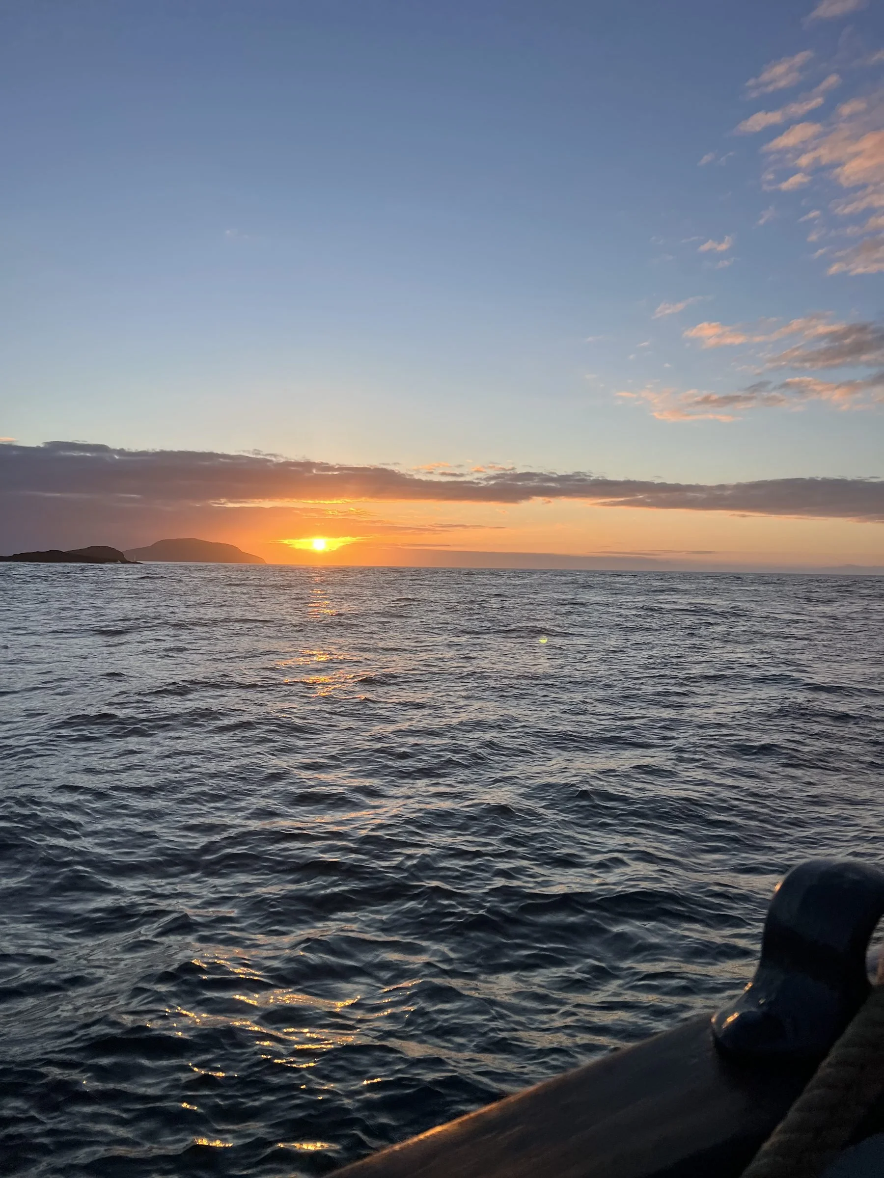 Sunset over the ocean with distant landforms on the horizon and a partly cloudy sky.