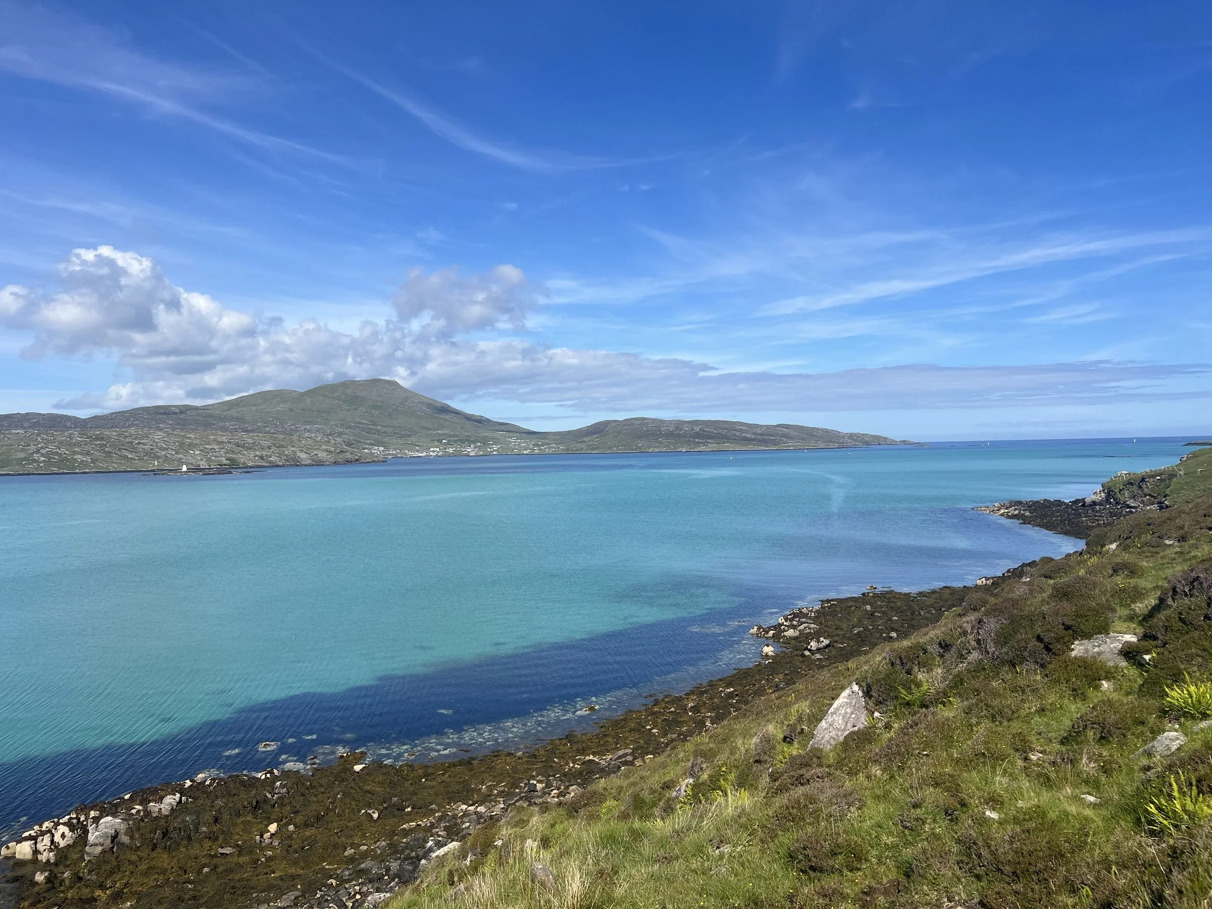 A scenic view of a large body of turquoise water with a hilly landmass in the background, under a partly cloudy blue sky.