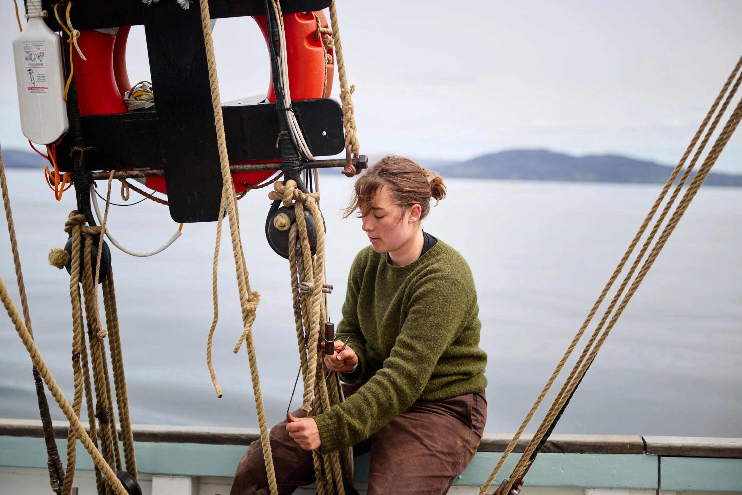 Crew member tying a rope on a Provident with a body of water and distant hills in the background.