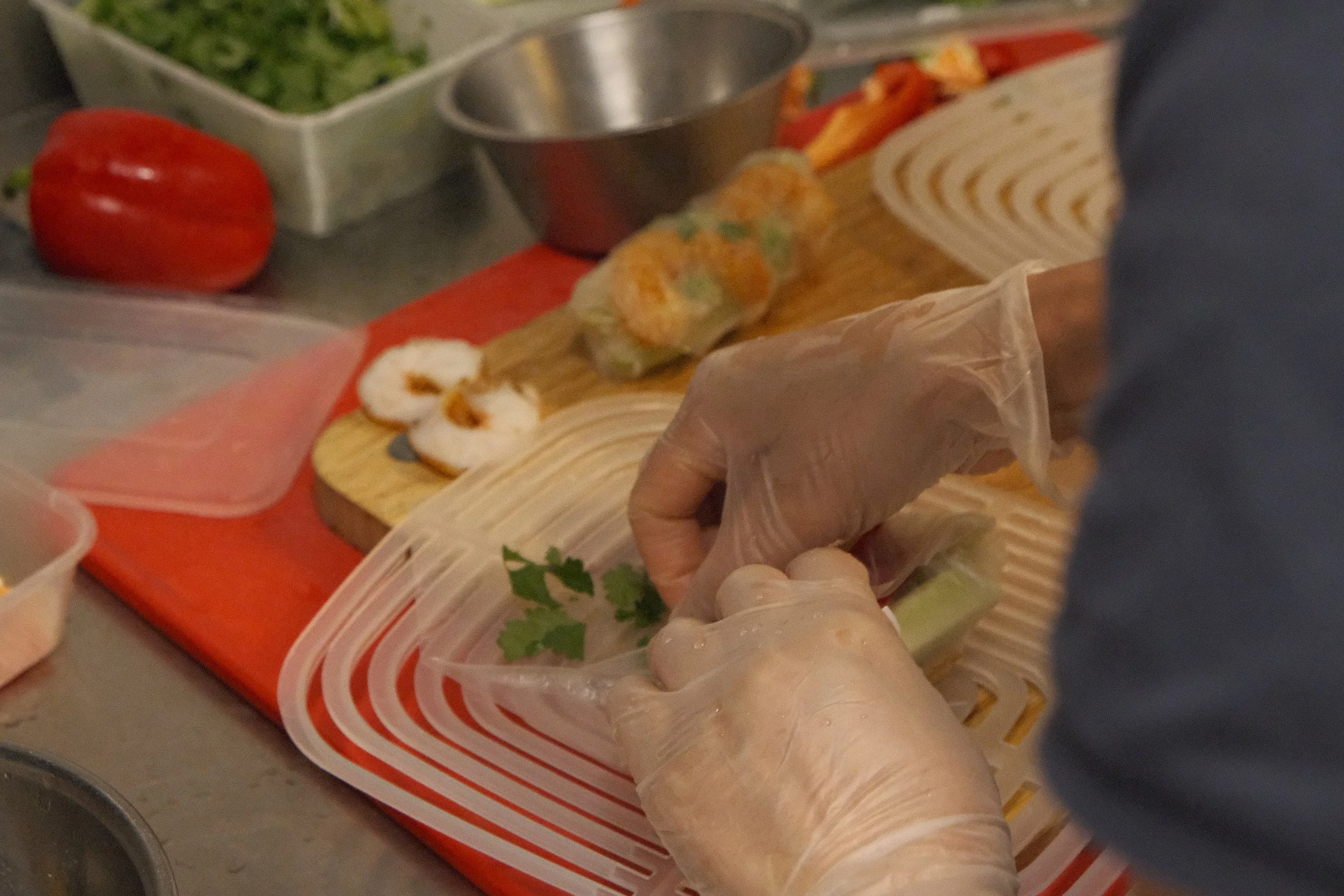Person som hanterar en wrapsrulle i en plasthandske, omgiven av grönsaker och andra ingredienser.