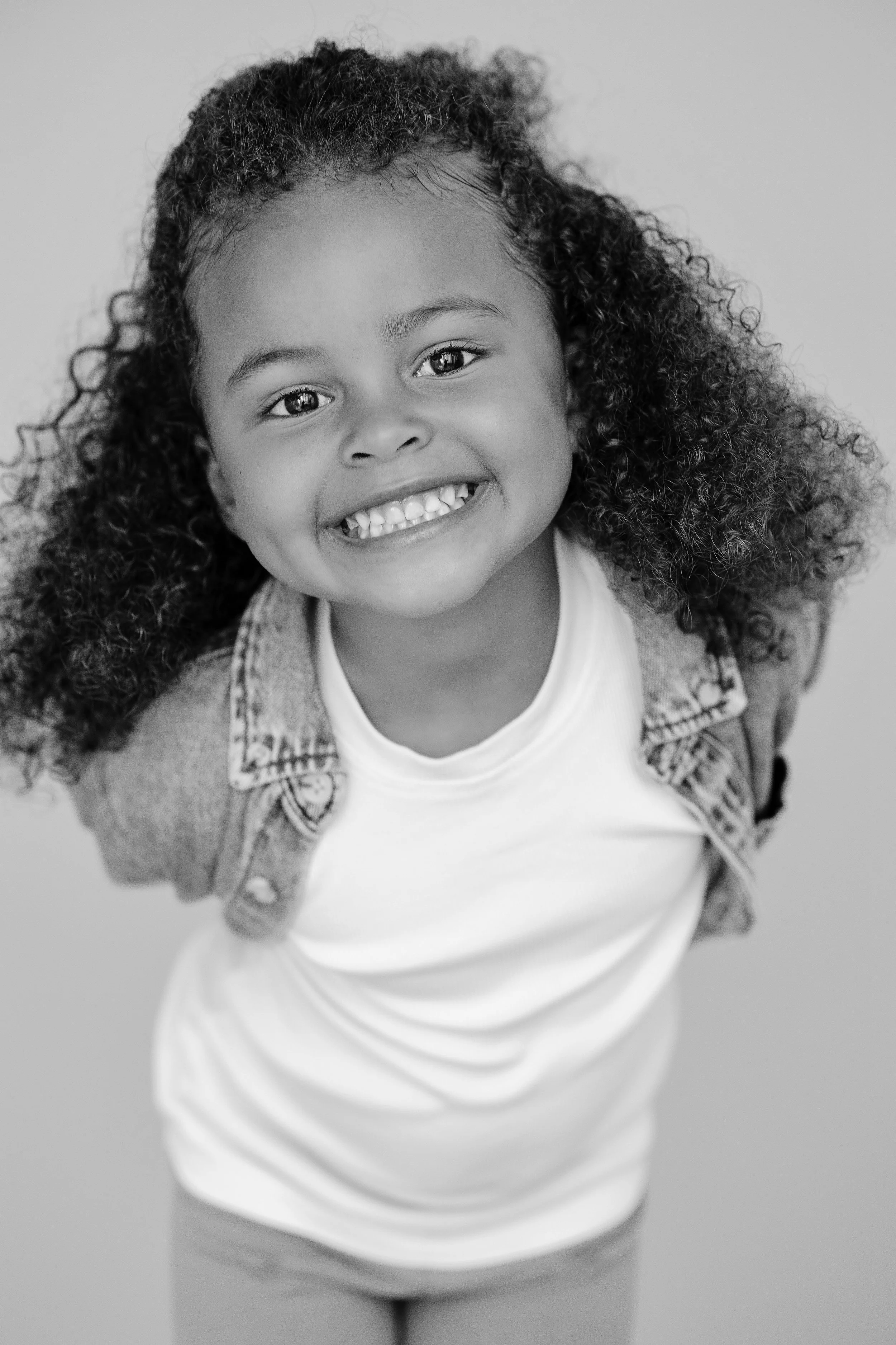 Smiling child model in a denim jacket during a natural headshot and model portfolio update session.
