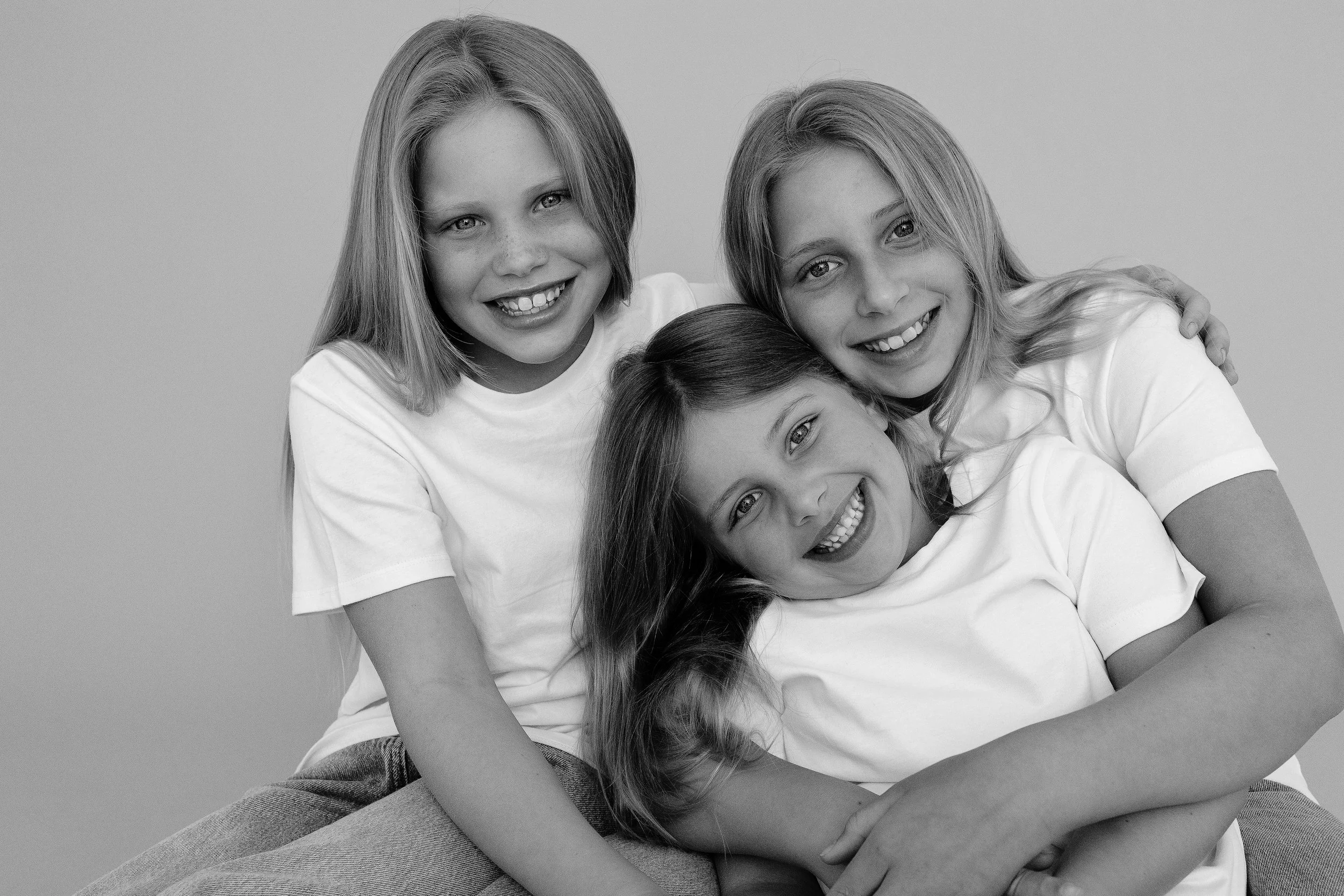Sisters smiling and cuddling together during a natural family photography session.
