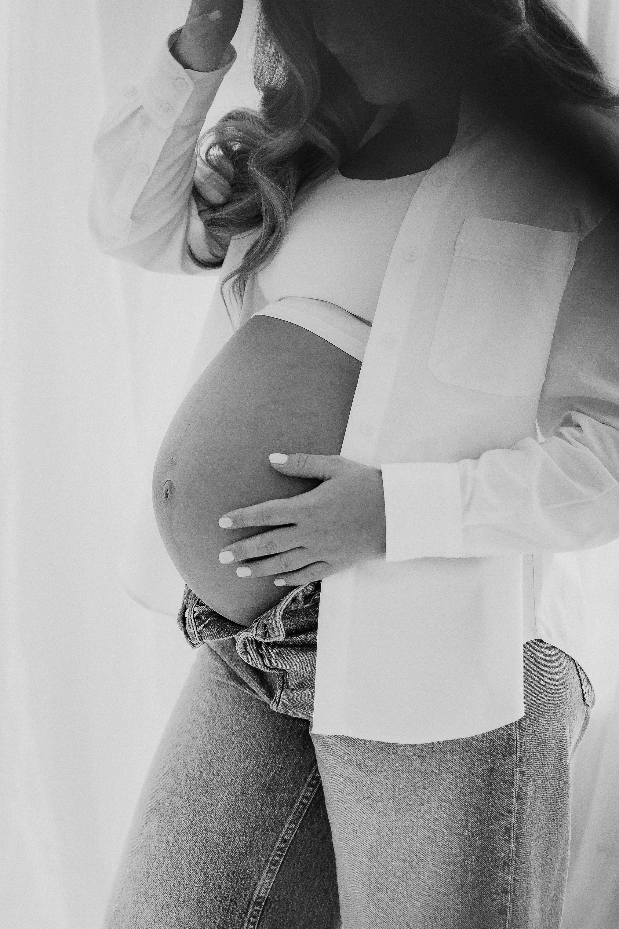 Pregnant woman cradling her baby bump during a natural maternity photoshoot in Bromley, Kent.