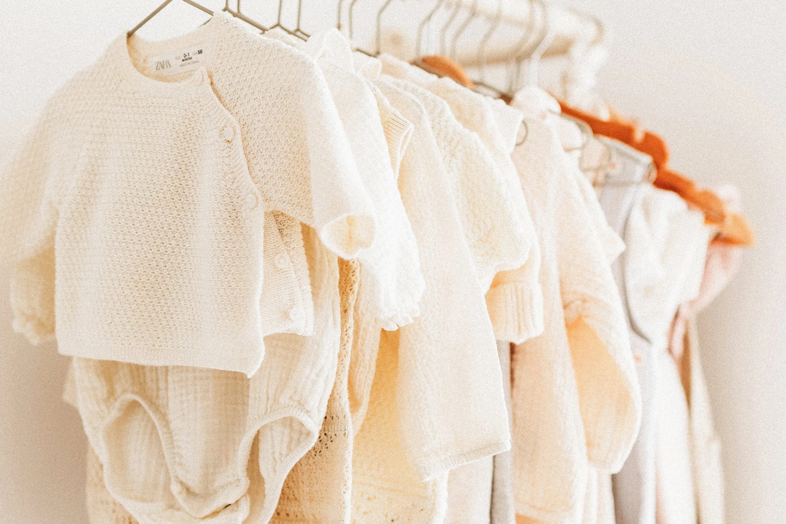 Cream-colored baby clothes hanging on hooks in a closet.