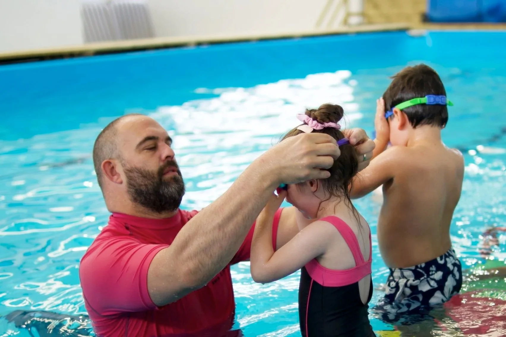 A swimming instructor helping young children with swimming skills in a swimming pool.