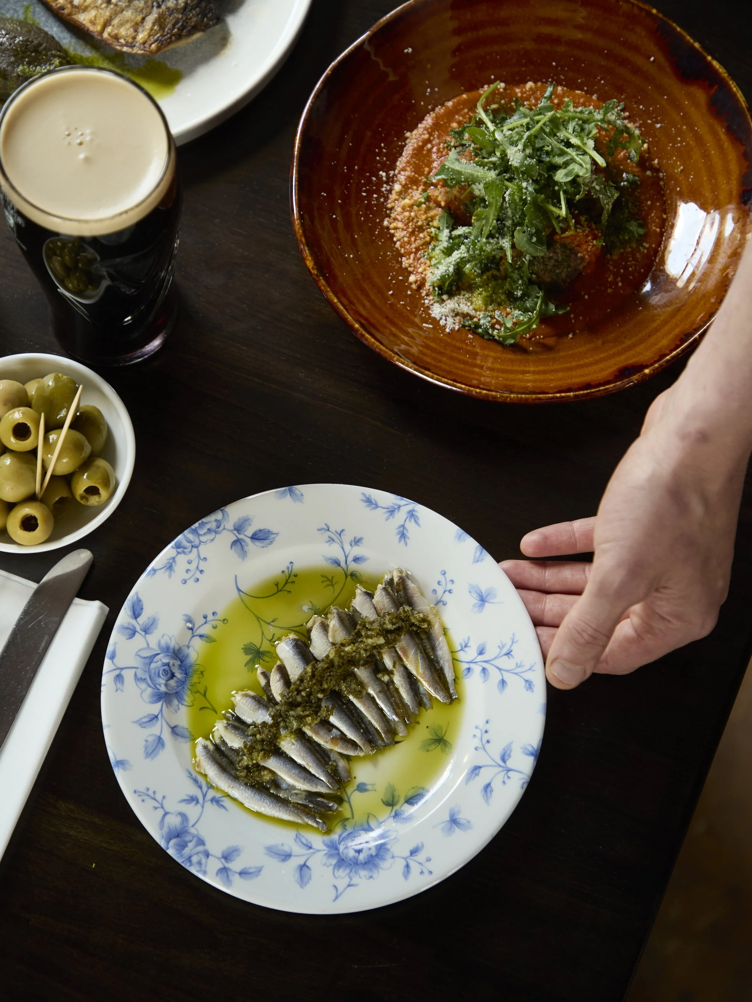 A plate of grilled sardines drizzled with oil and topped with herbs, served on a blue and white floral plate.