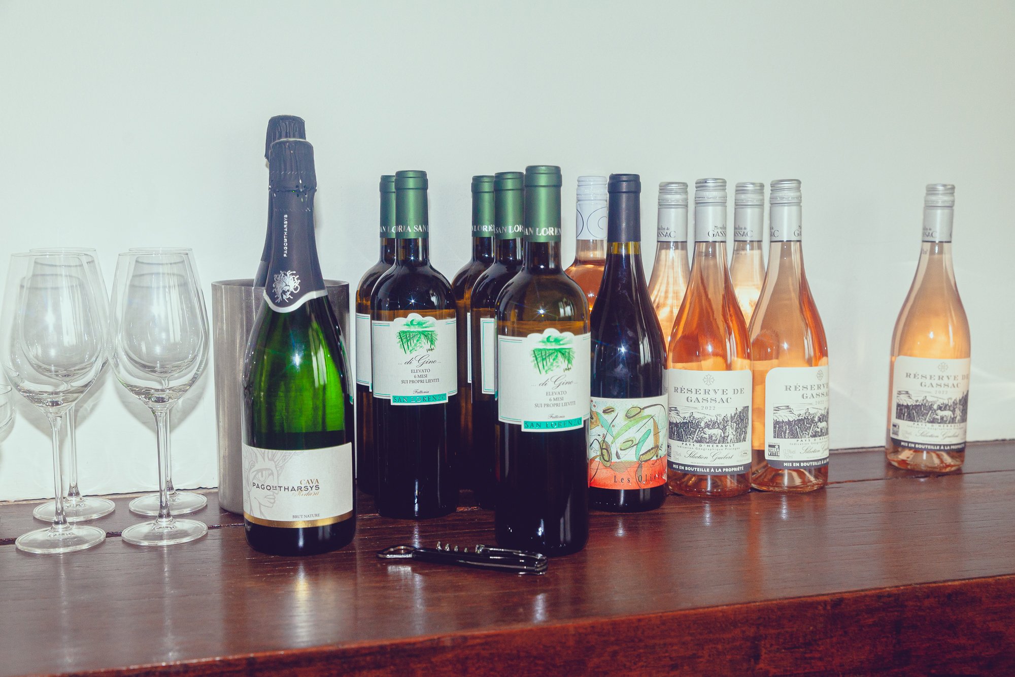Various bottles of wine and champagne along with empty wine glasses on a wooden surface.