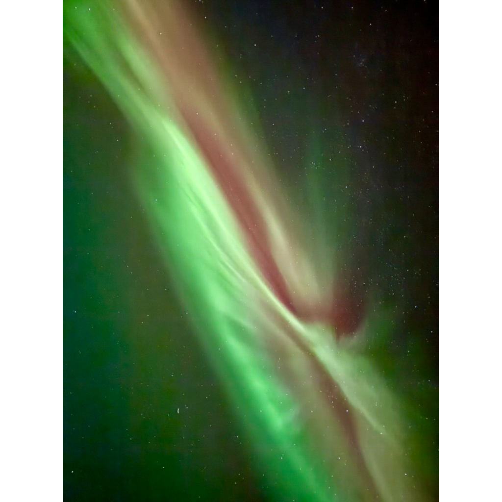 Diagonal ribbons of lime-green and magenta aurora across a dense star field