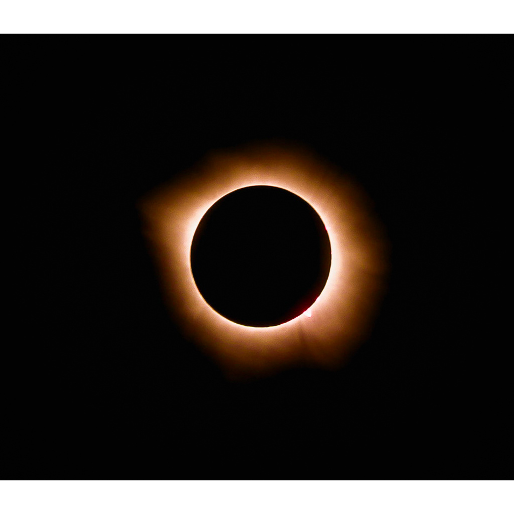 Total solar eclipse with a black lunar disk ringed by a glowing amber corona against a black sky