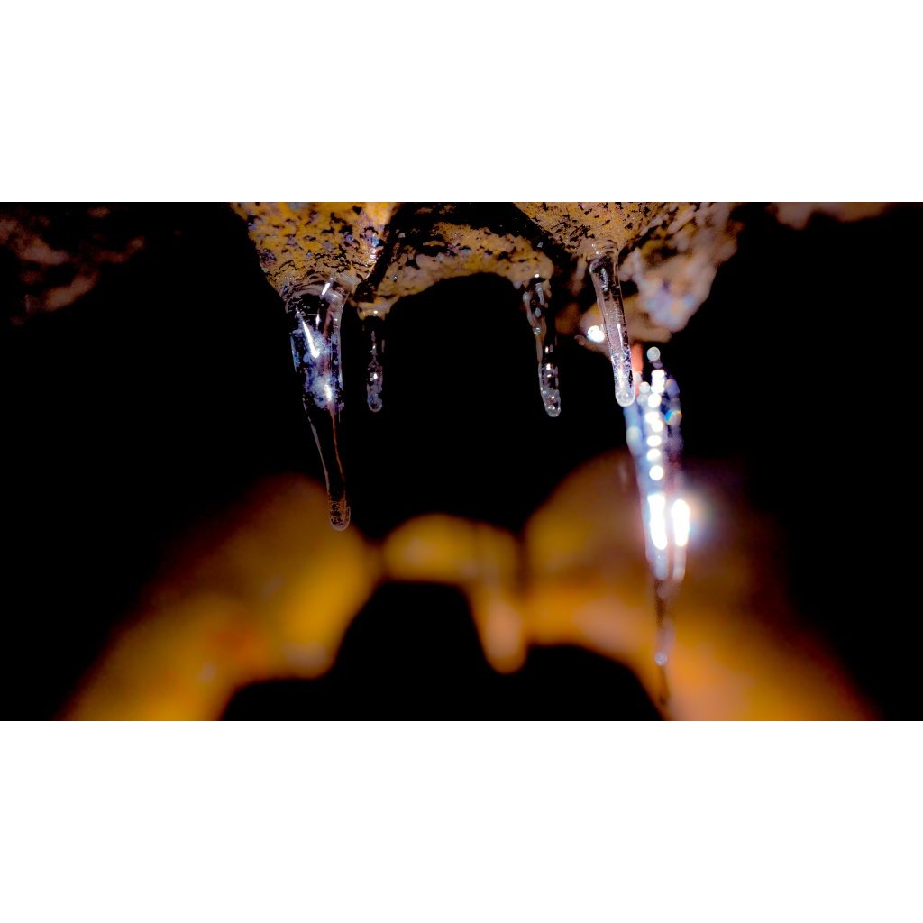 Close-up of translucent icicles hanging from dark rock with warm amber light glowing behind them