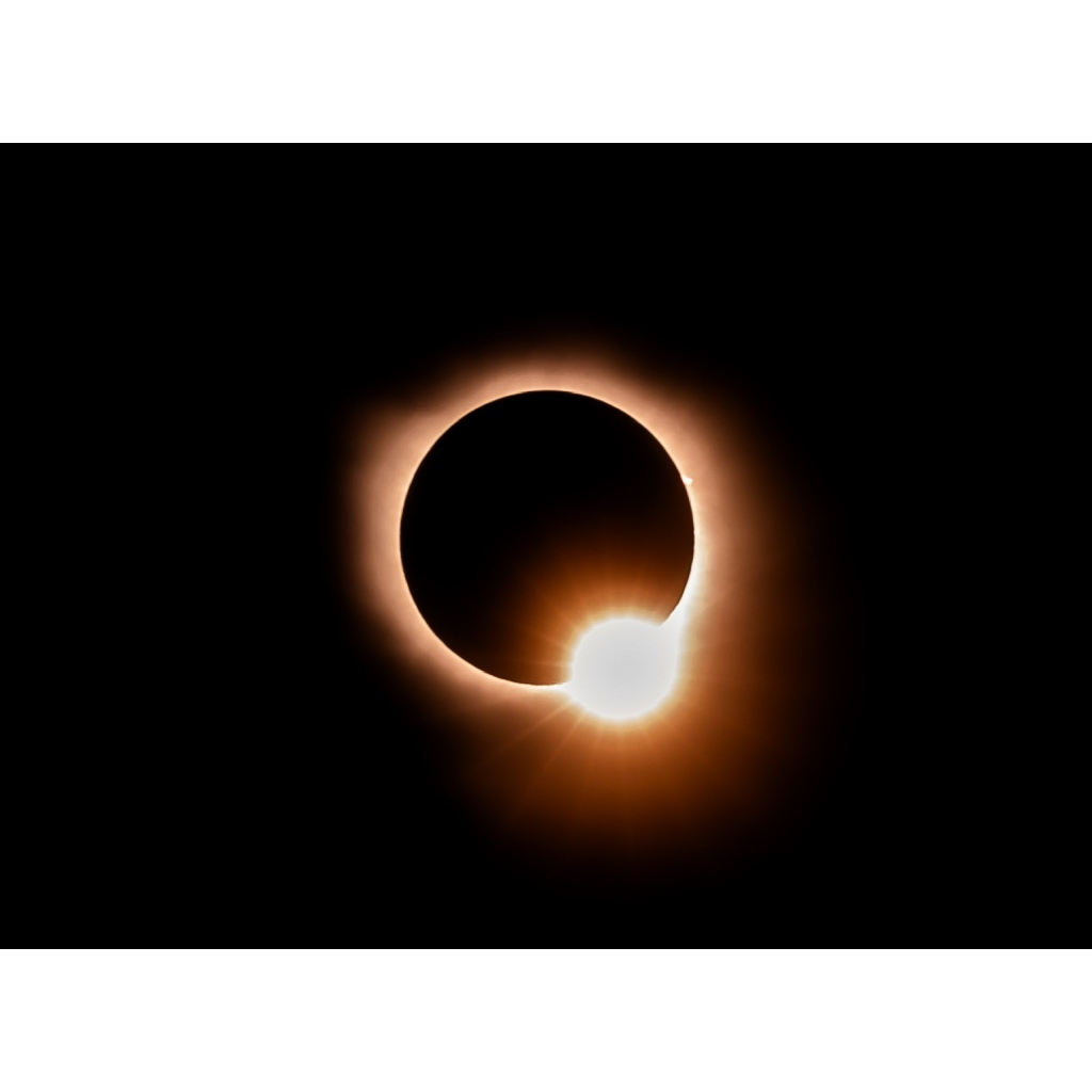 Solar eclipse diamond-ring effect with a bright flare on the moon’s edge and a warm amber corona