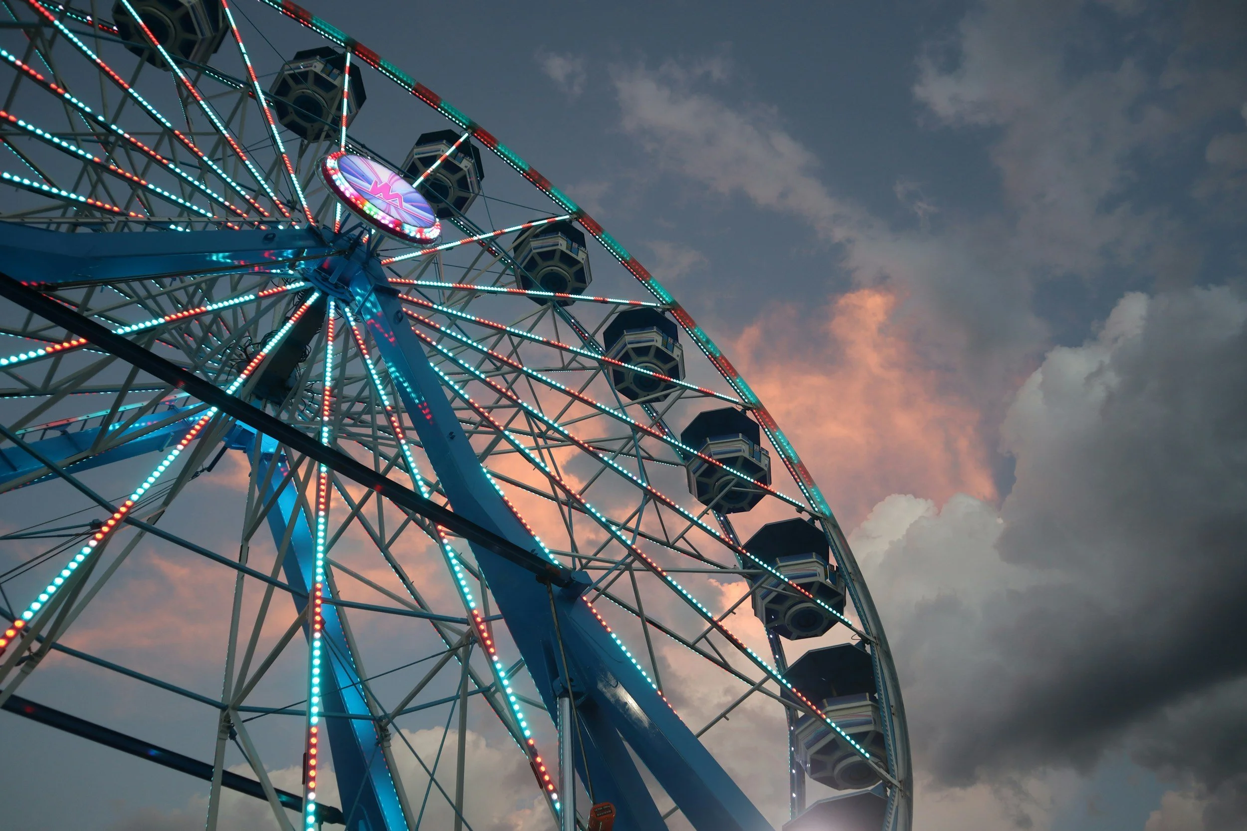 A large, illuminated Ferris wheel with colorful lights against a cloudy evening sky.