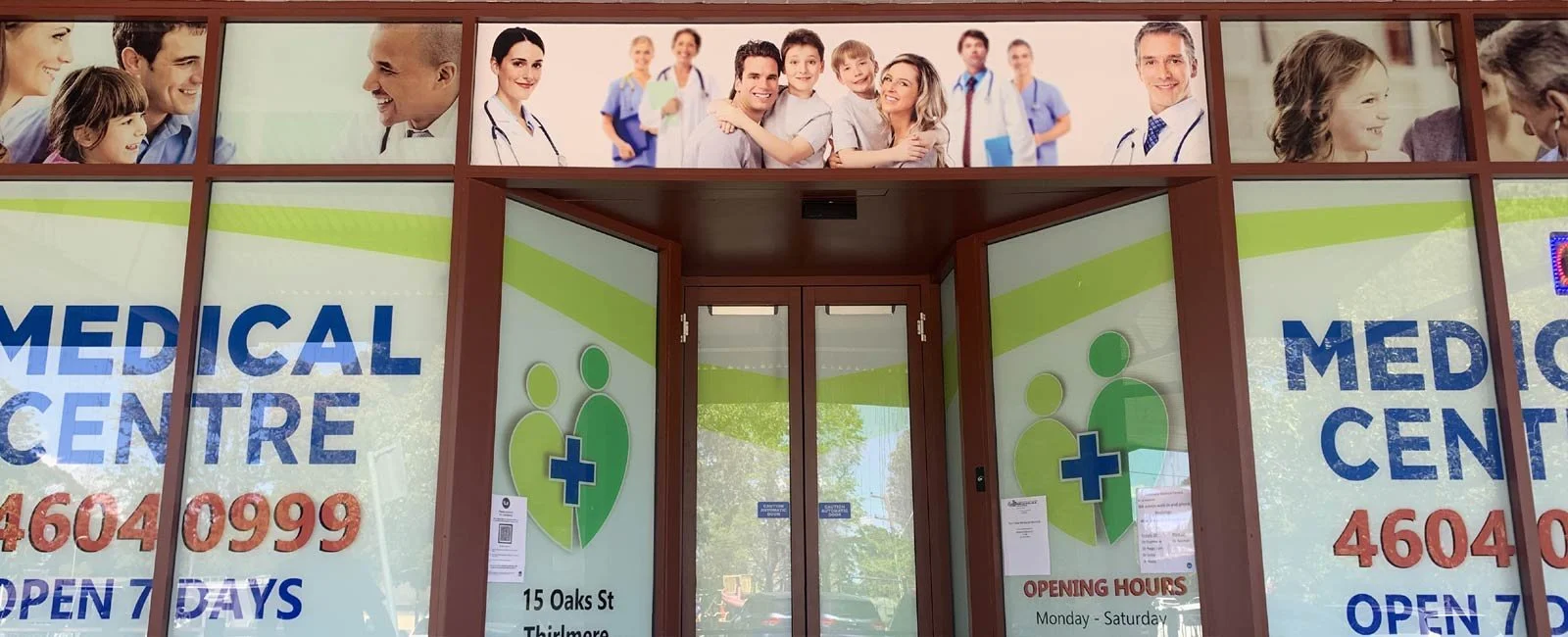 Front view of a medical center entrance with signs indicating its services, address, contact number, and opening hours.