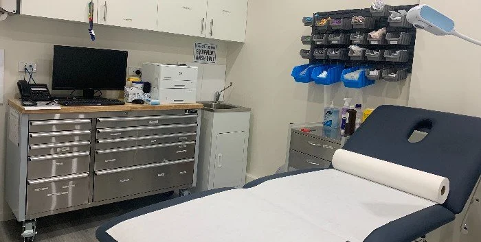 Medical examination room with a treatment bed, a countertop with medical supplies, a computer, and cabinets.