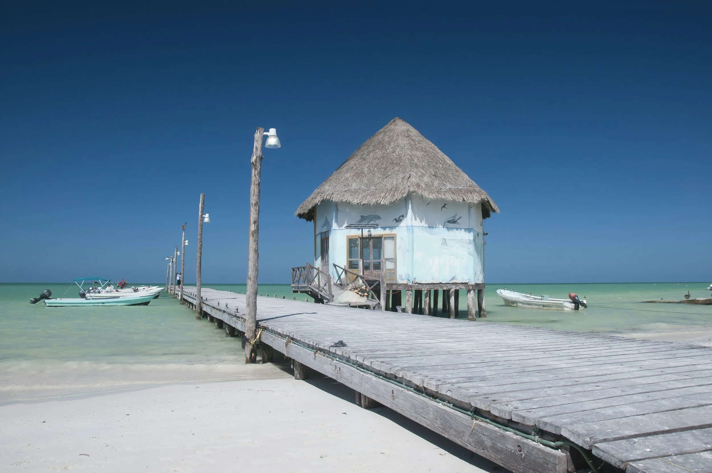 Thatched-roof bungalows over turquoise Caribbean water in Holbox.