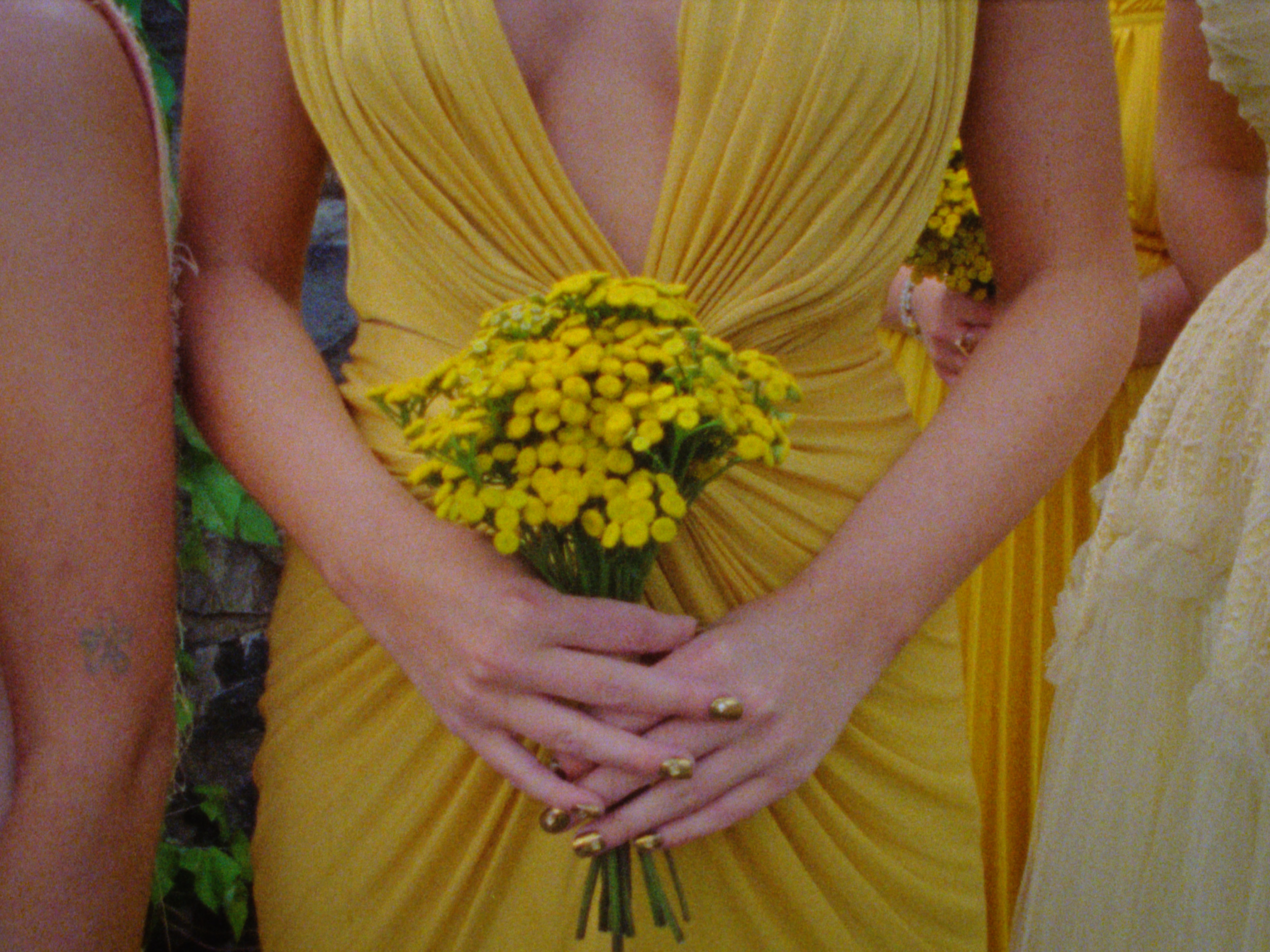 Person in a yellow dress holding a yellow bouquet of flowers, with arms crossed in front of her.