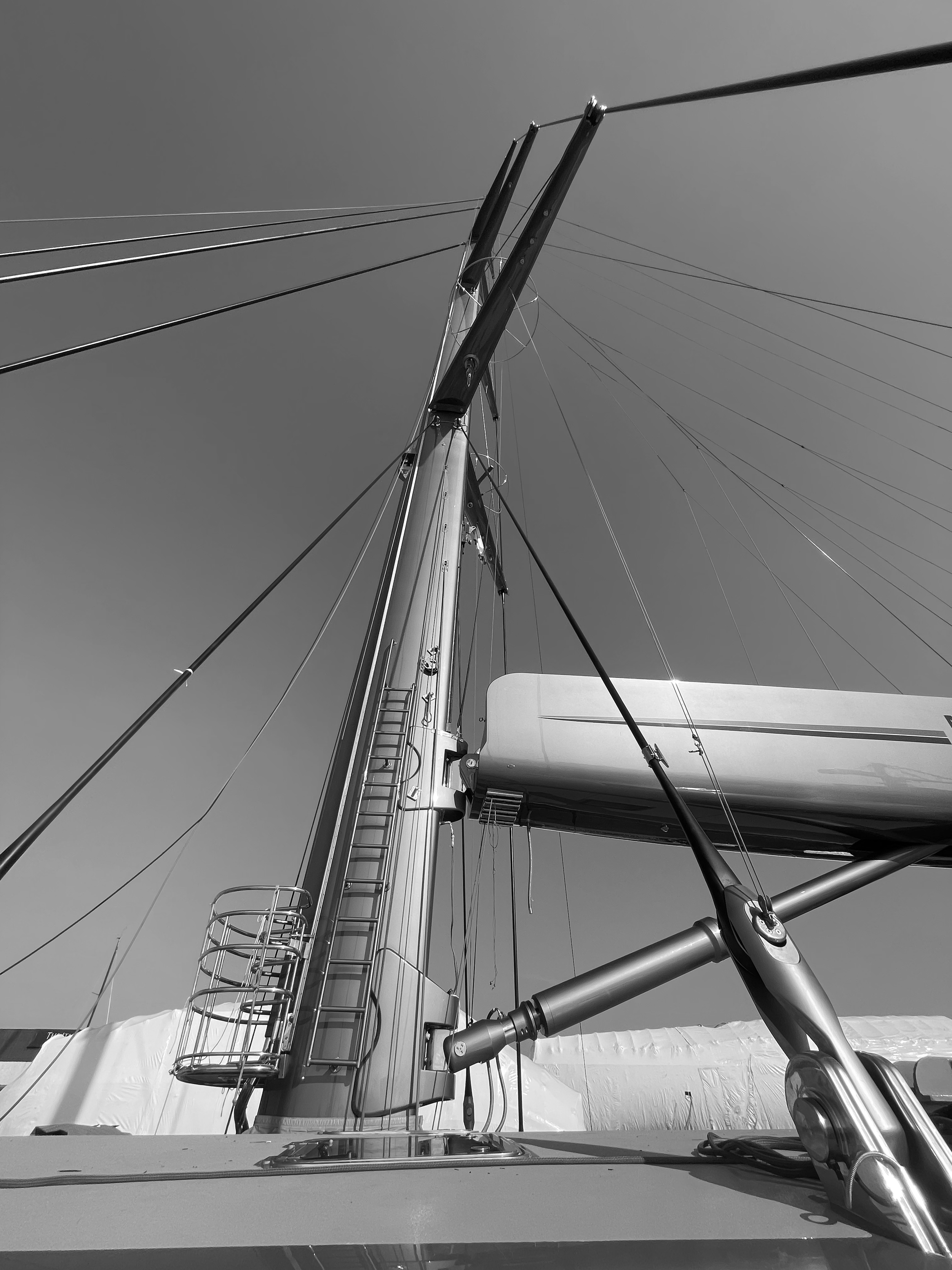 Looking up at a sailboat mast with rigging and hardware against a cloudy sky.