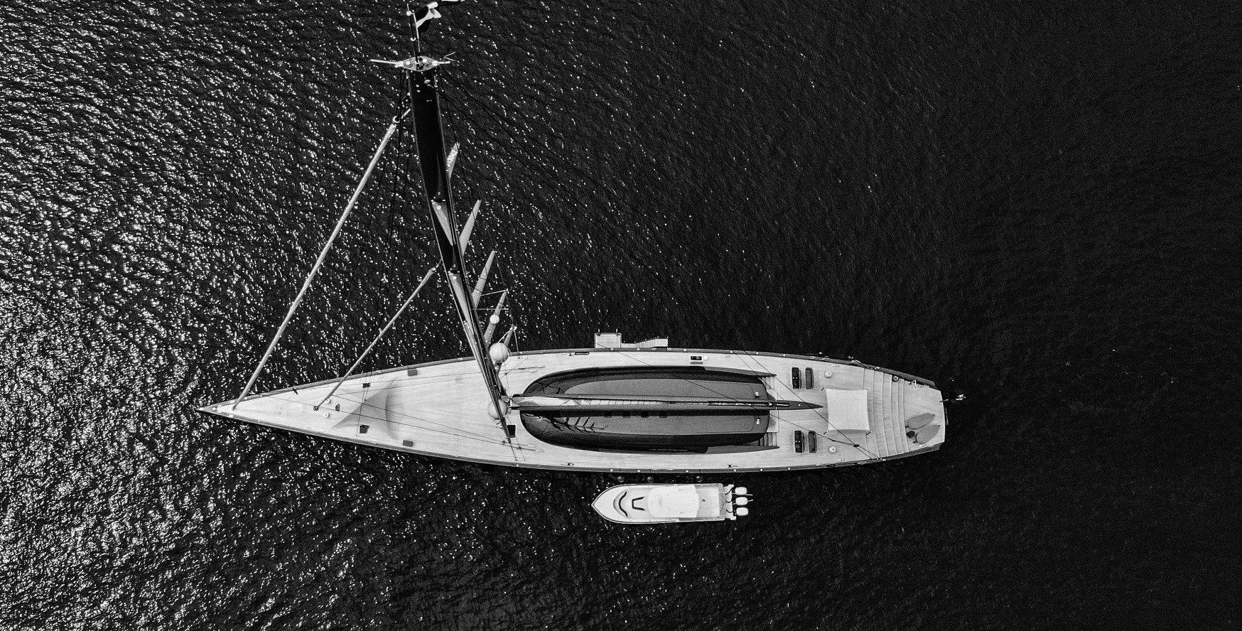 Aerial view of a sailboat with a smaller motorboat attached, floating on dark water.