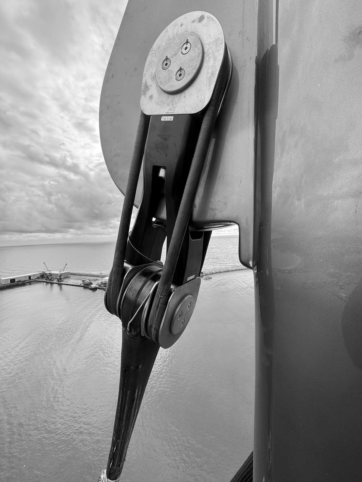 Close-up of helicopter rotor hub with rigging and hydraulic components, over a body of water with a coastline and cloudy sky in the background.