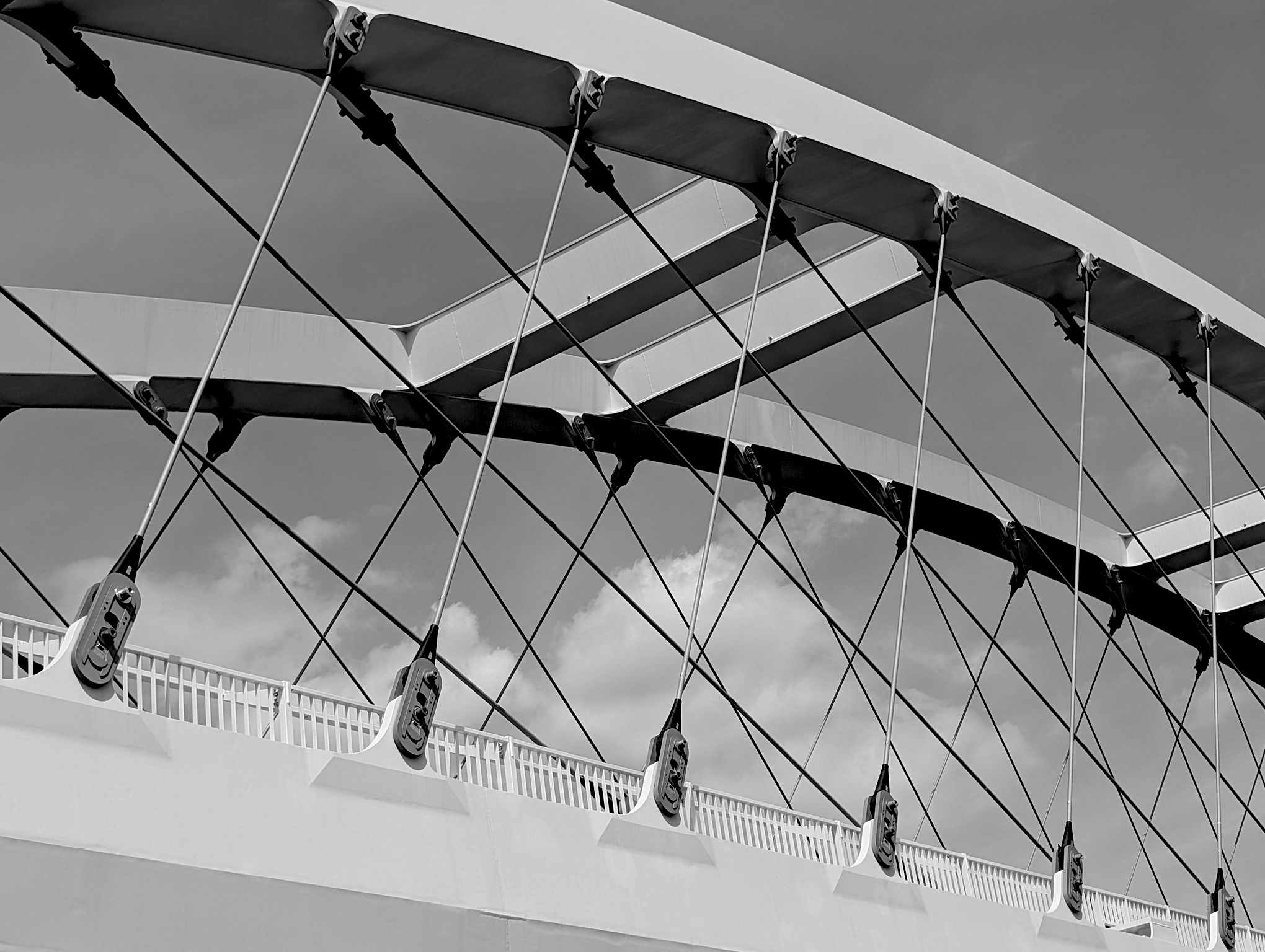 Close-up photo of modern building with architectural design, featuring railings, support cables, and shading structures against a cloudy sky