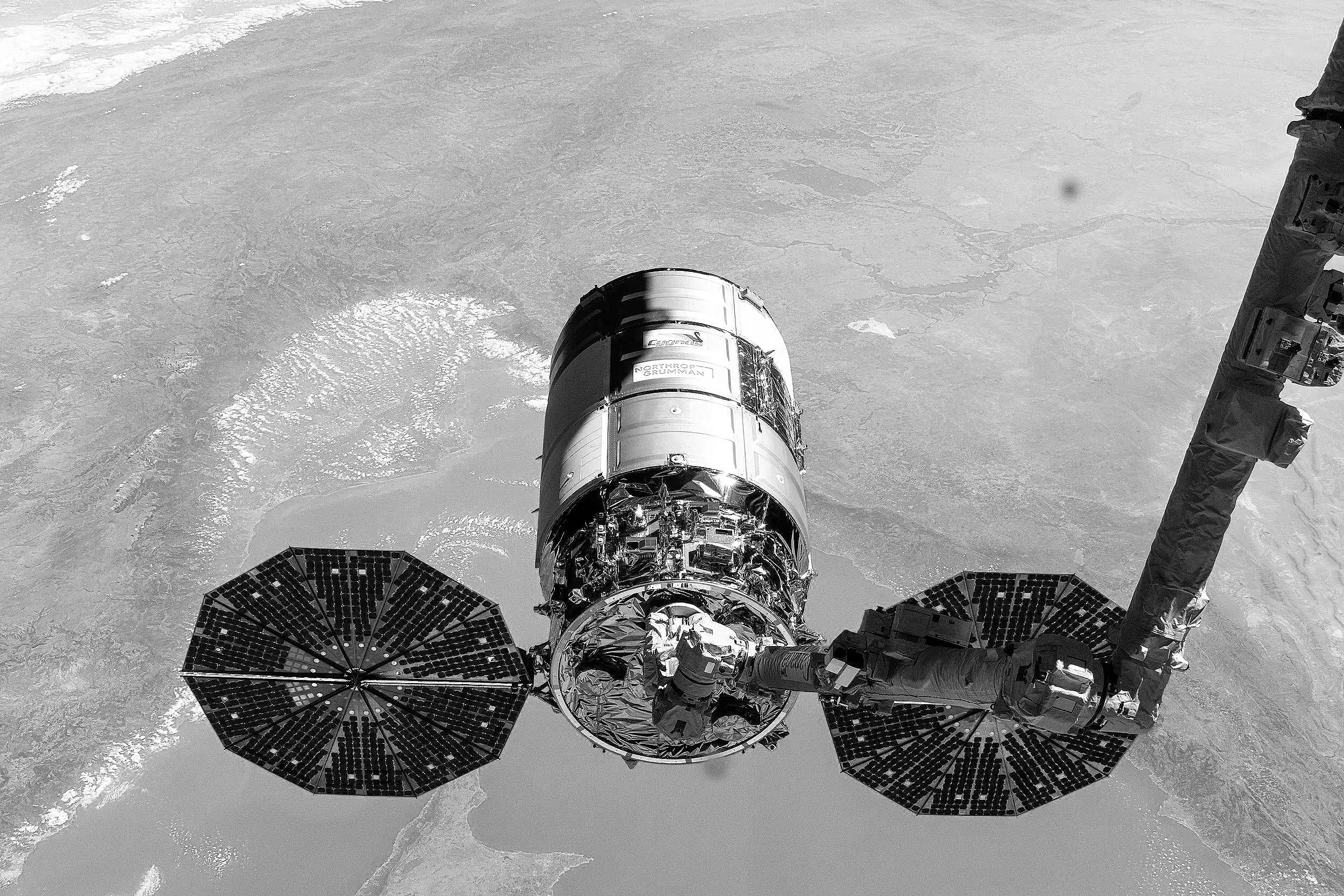 View of a satellite or spacecraft component with solar panels, orbiting above Earth’s surface, which appears as a textured, icy landscape.