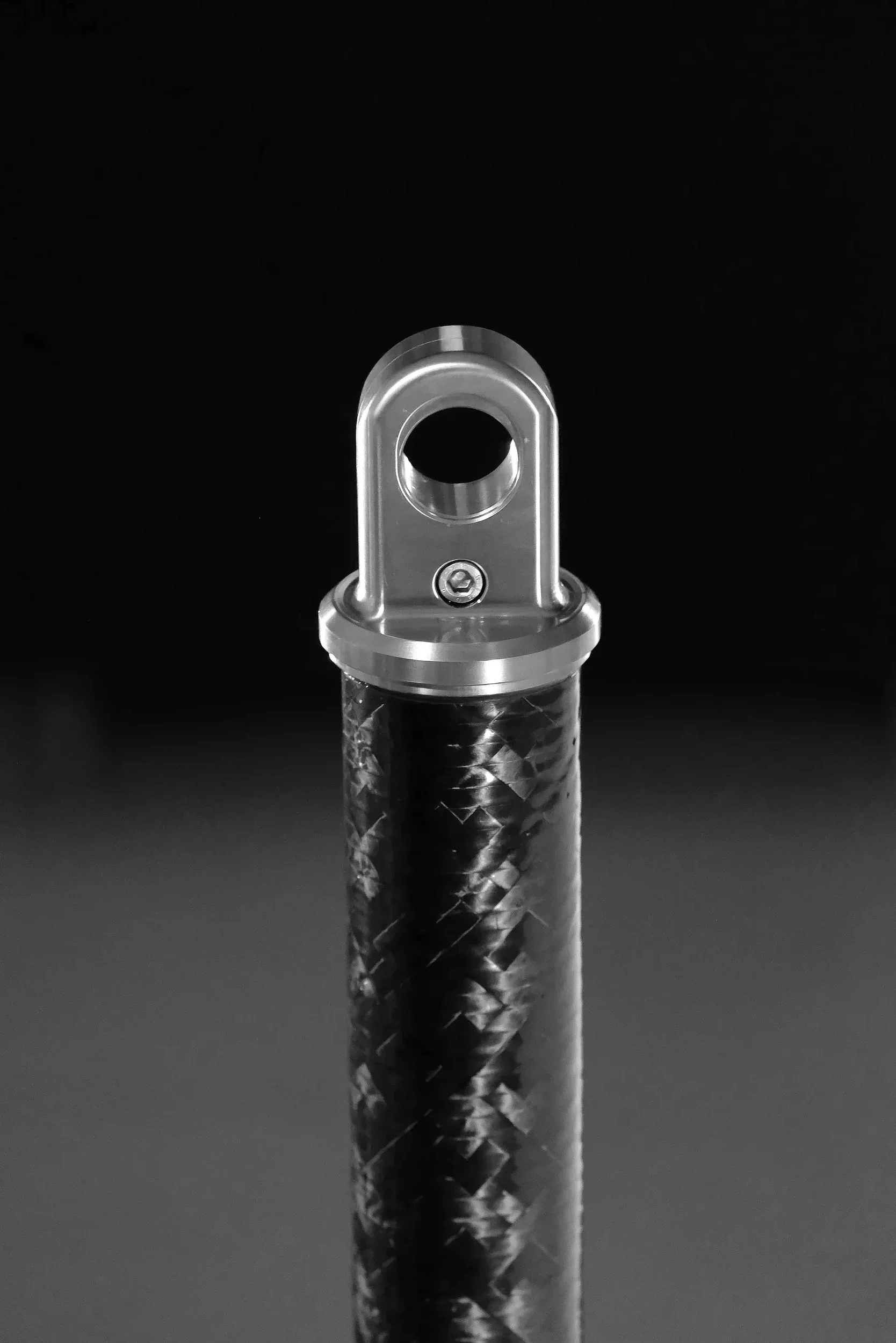 Close-up image of a metallic object with a circular hole at the top, mounted on a textured cylindrical stand against a black background.