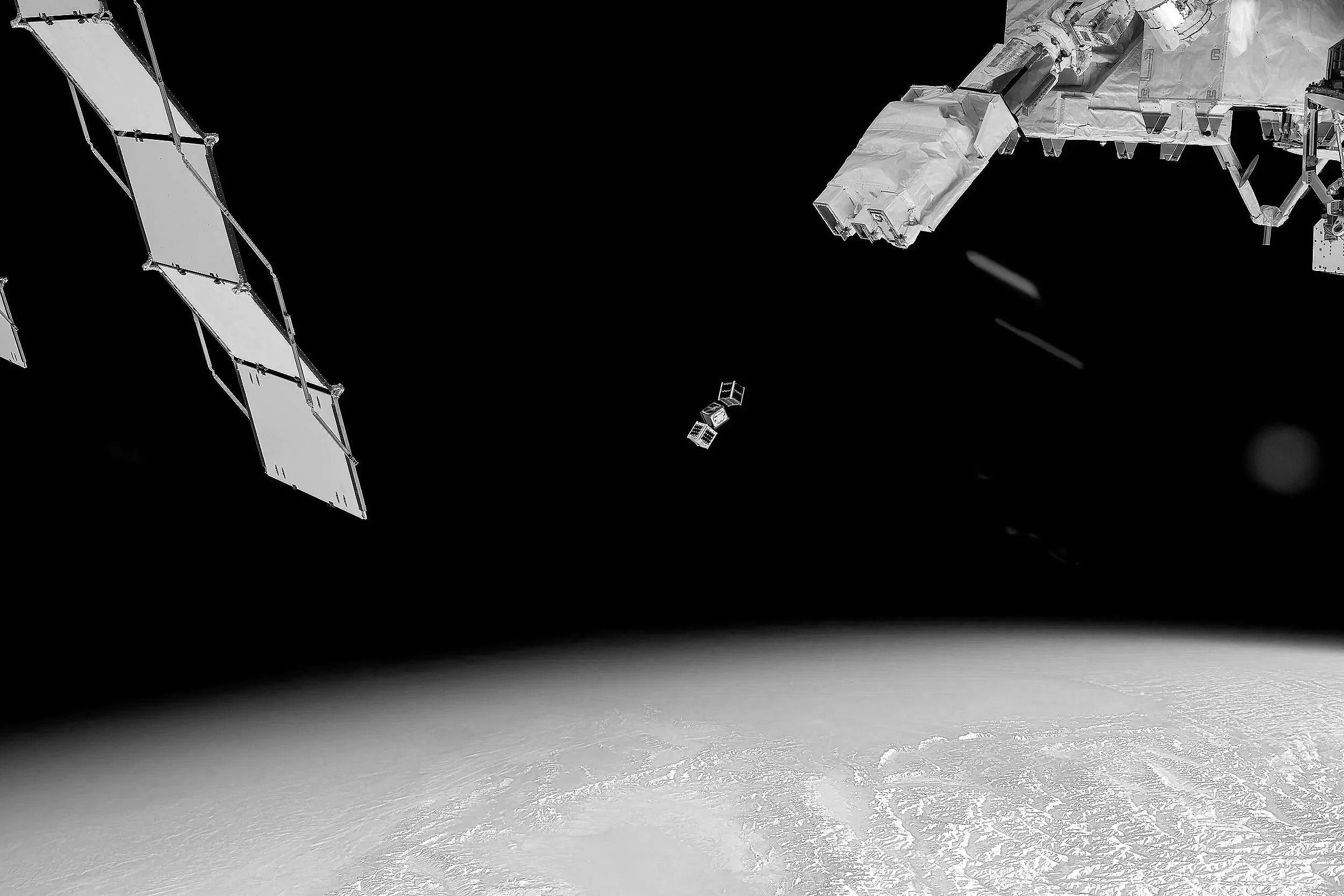 View of space station modules orbiting Earth viewed from space, with parts of the station extending into darkness and Earth’s surface visible below.