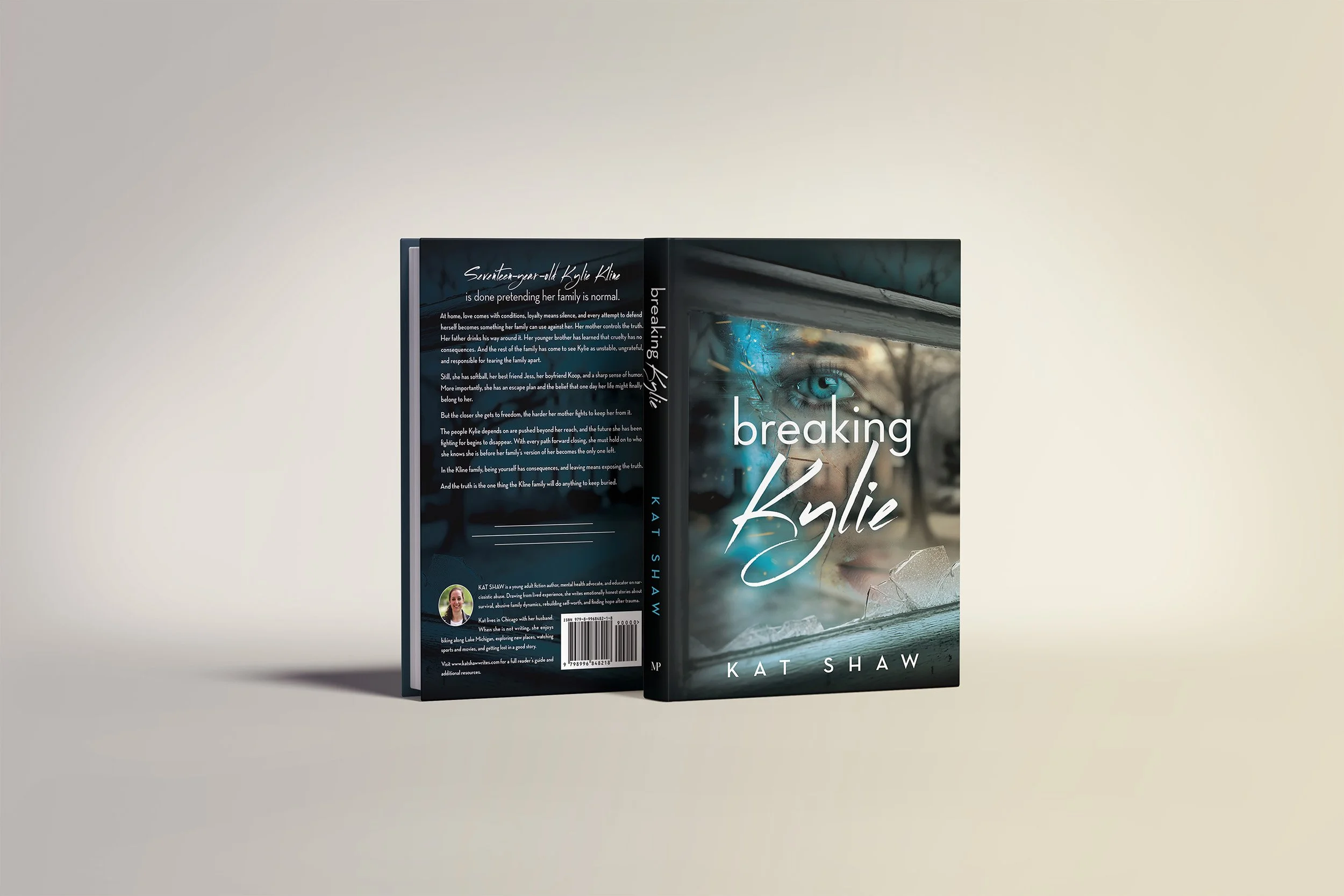 A hardcover book titled "Breaking Kylie" by Kat Shaw, with a cover image of a woman with blue eyes, a cracked window, and a tree outside, stands upright against a plain light-colored background. The back cover contains a synopsis and author information.