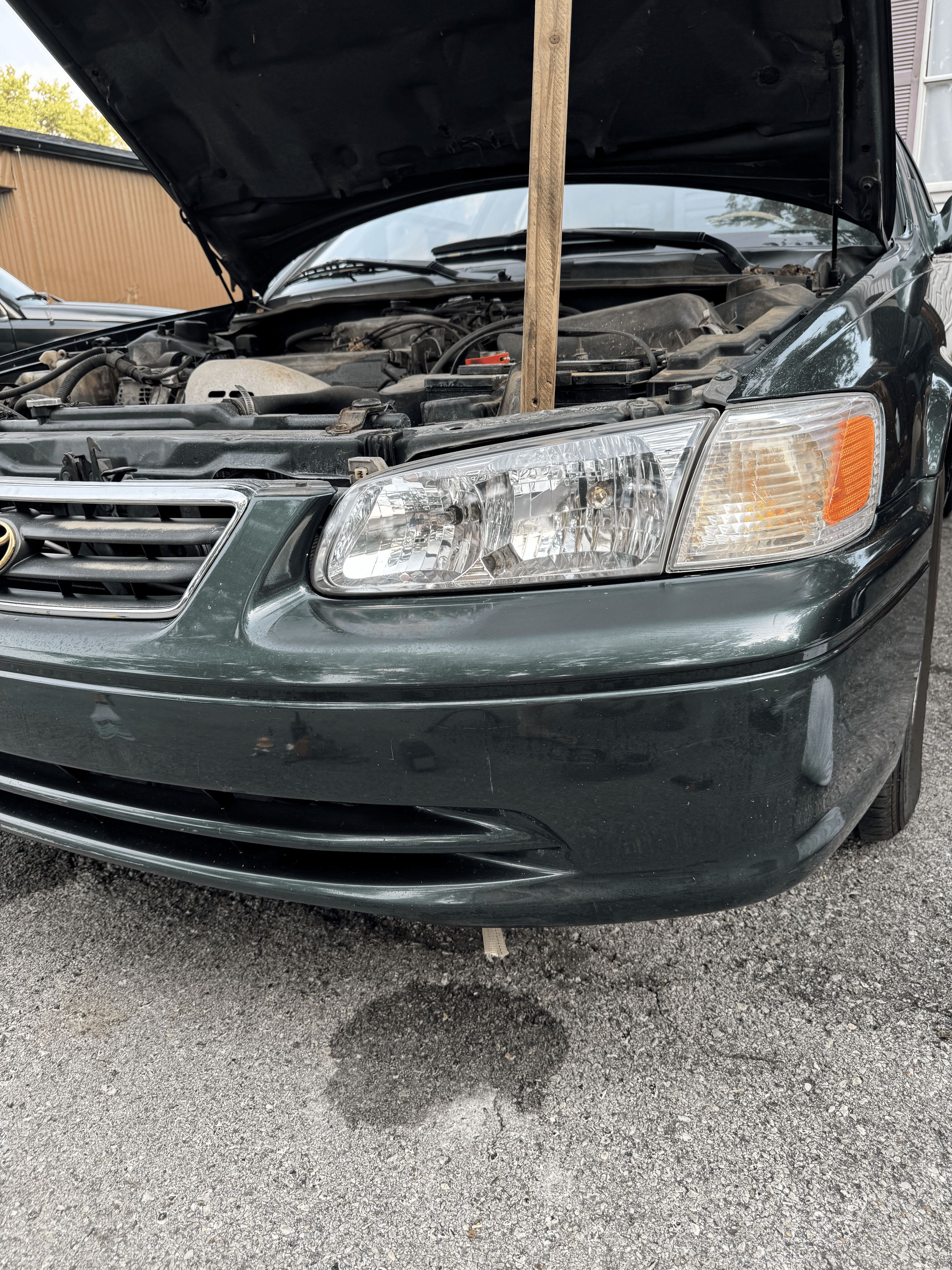 A dark-colored car with its hood open, sporting newly restored headlights.