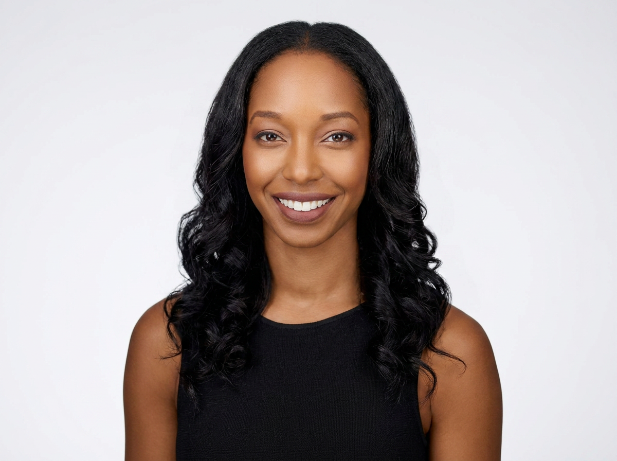A woman with wavy black hair smiling in a black sleeveless top, standing against a white background.