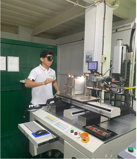 A man wearing safety glasses working on a scientific machine in a lab.