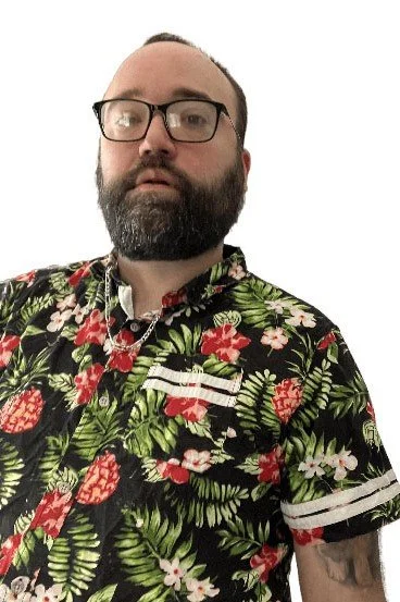 A man with glasses and a beard wearing a tropical floral shirt, standing against a plain white background.