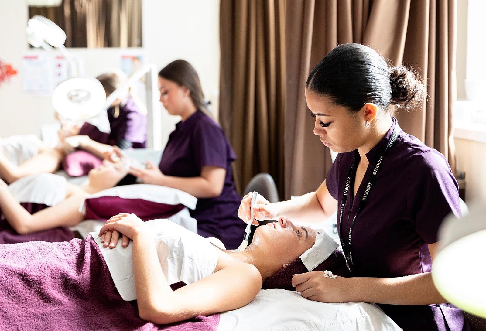 A nurse or cosmetologist sedates a woman lying on a treatment table with an oxygen mask, while two other nurses or cosmetologists work on similar patients in the background, in a clinical or training room.
